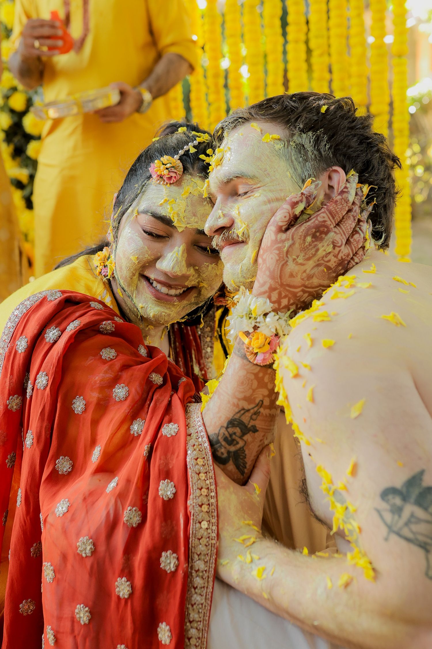 A couple in traditional Indian wedding attire share a joyful moment during their haldi ceremony with yellow turmeric decorations.