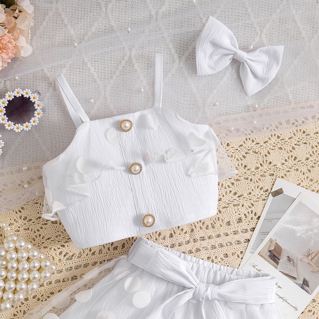 Close-up of white baby outfit with button details and matching tulle skirt set on lace fabric surface.