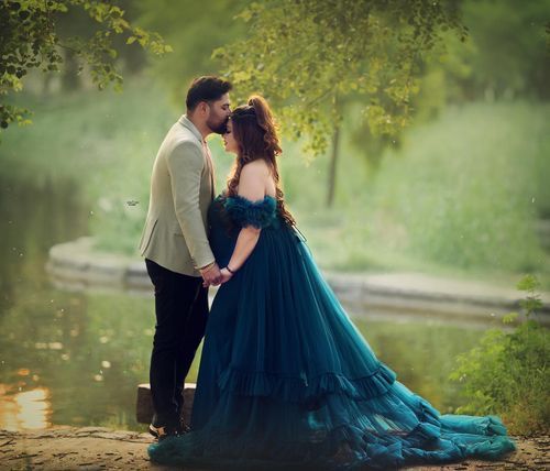 Romantic couple in formal attire embracing near pond with green foliage background.