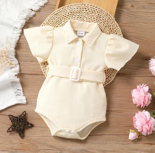 Cream colored baby romper with ruffled details displayed on wooden surface with floral accents.