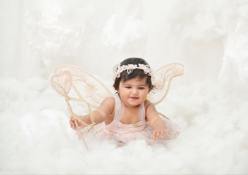 Dreamy baby photography of small child wearing fairy wings on cloudy white background.