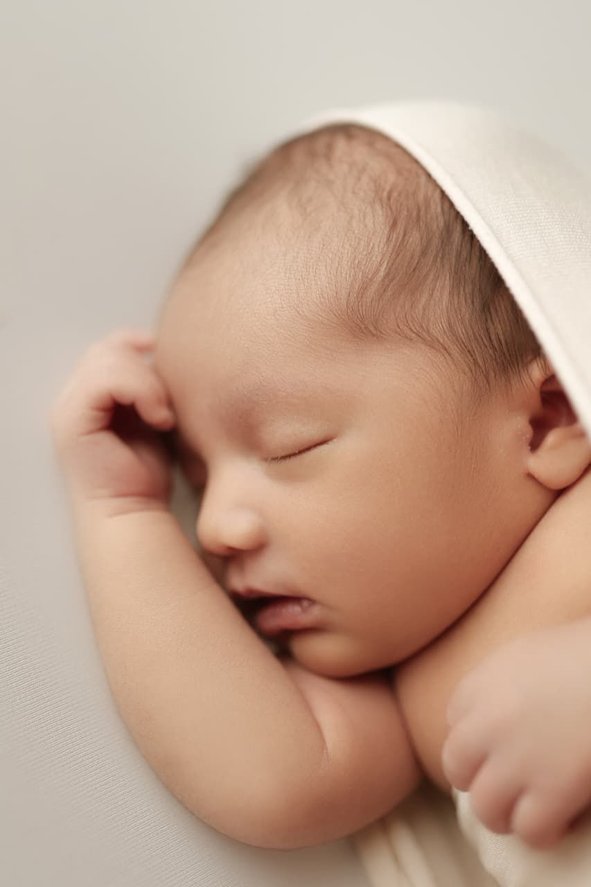 Peaceful newborn baby sleeping soundly, wrapped in a soft white blanket, with tiny hands tucked under cheek.