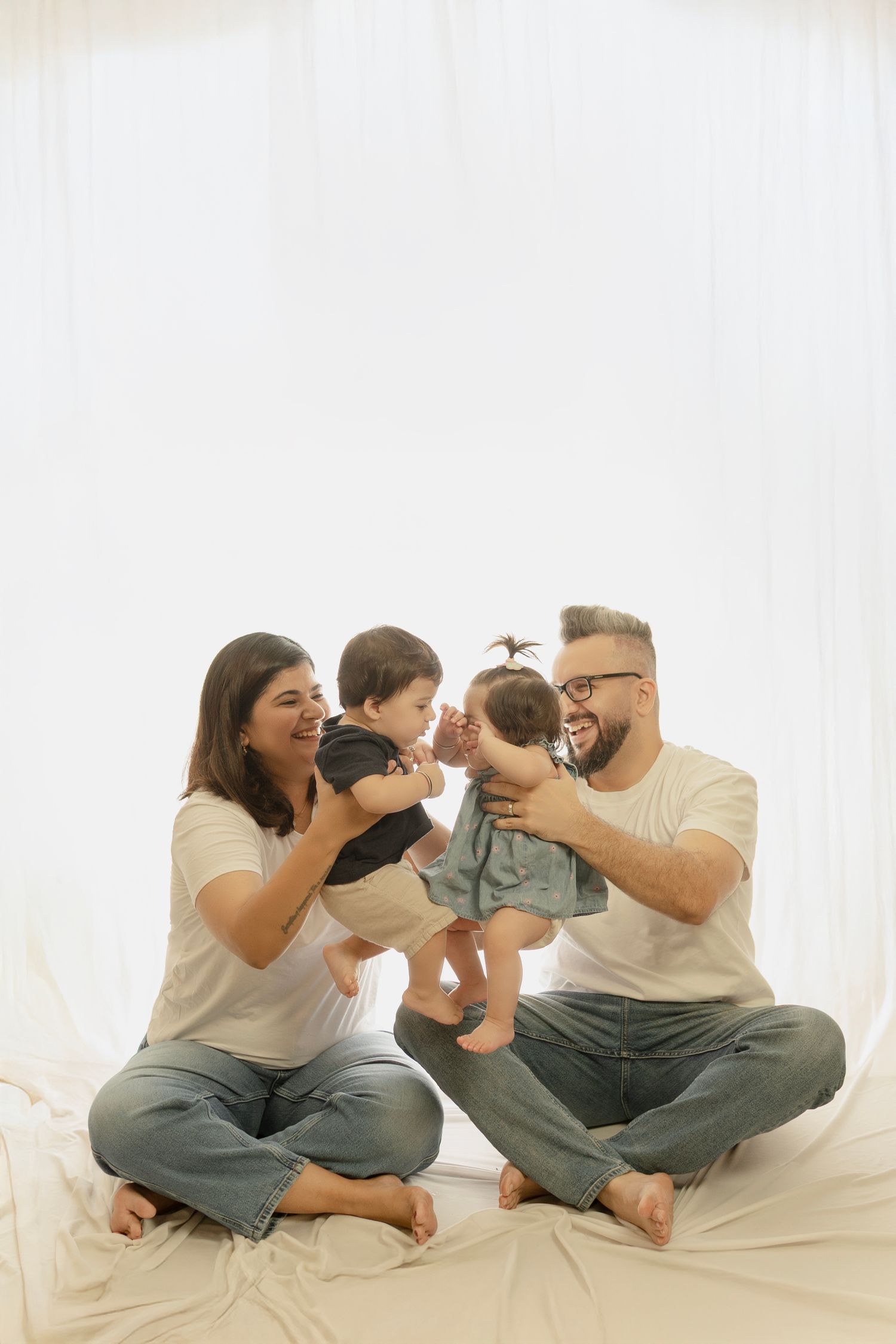 Family plays and interacts while sitting on white fabric in matching casual outfits.