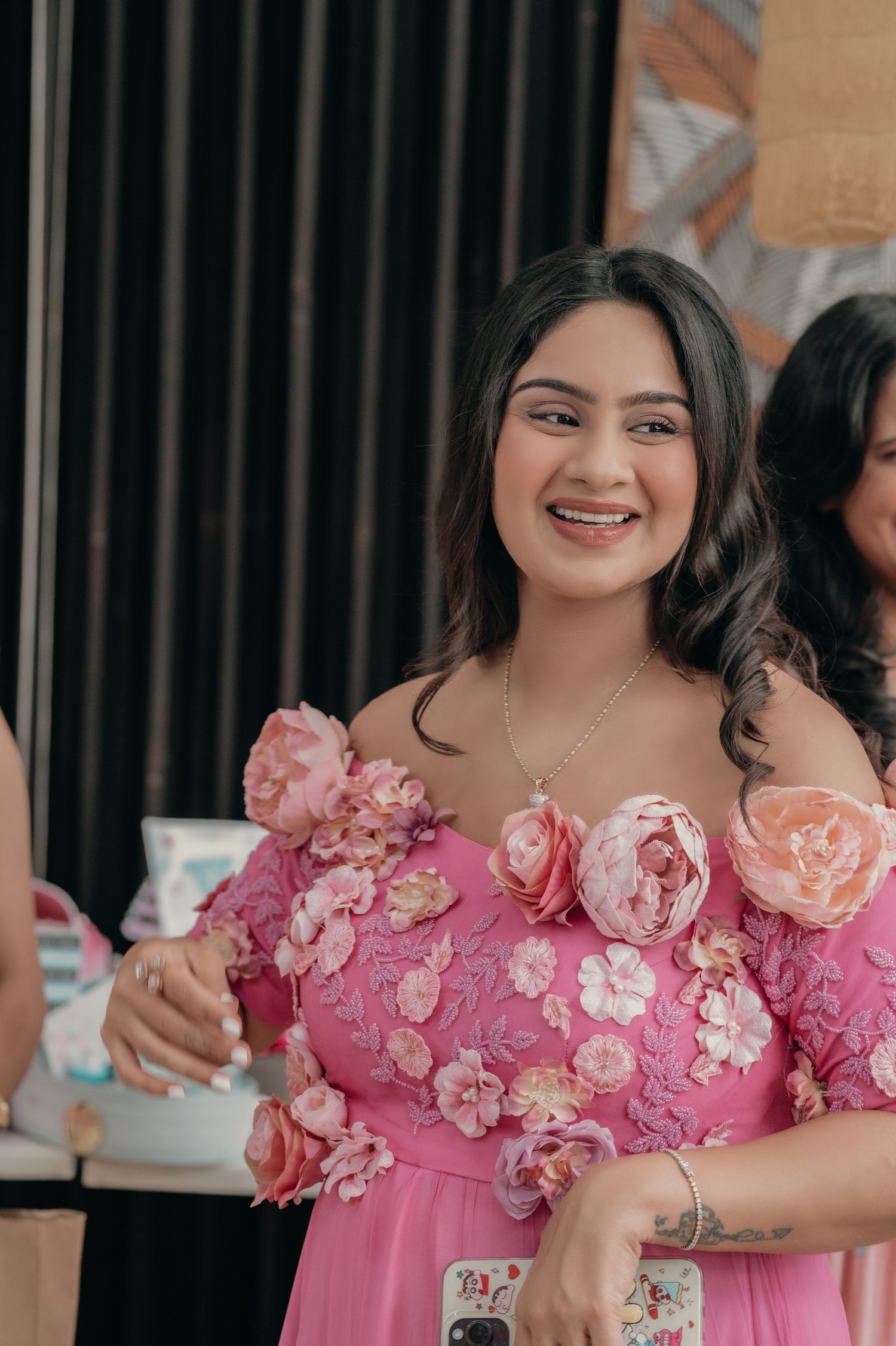 Smiling woman in a pink off-shoulder floral applique gown at a festive event.