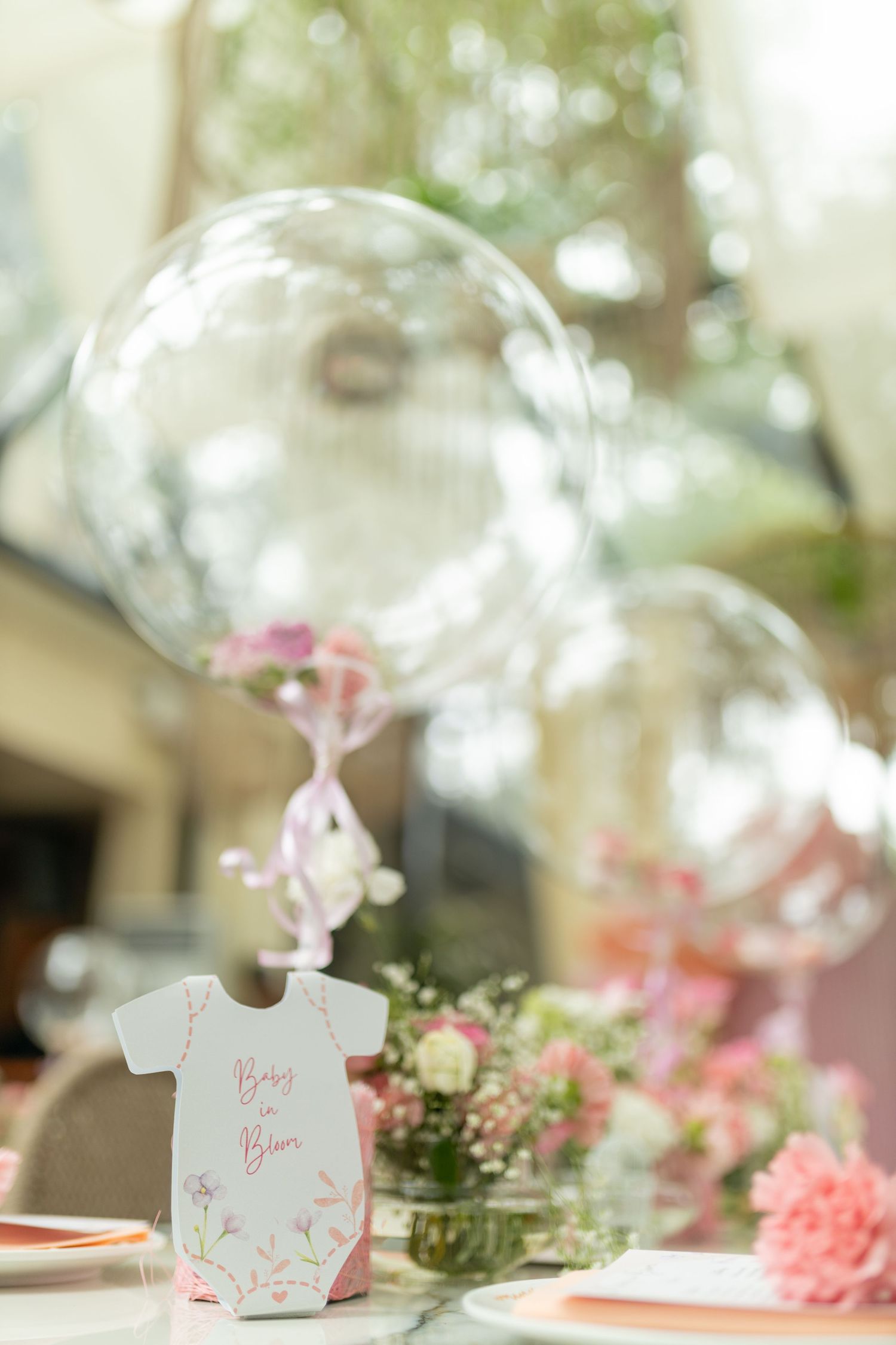 Baby in Bloom baby shower table decor with clear bubble balloons, pink floral arrangements, and onesie-shaped place cards.