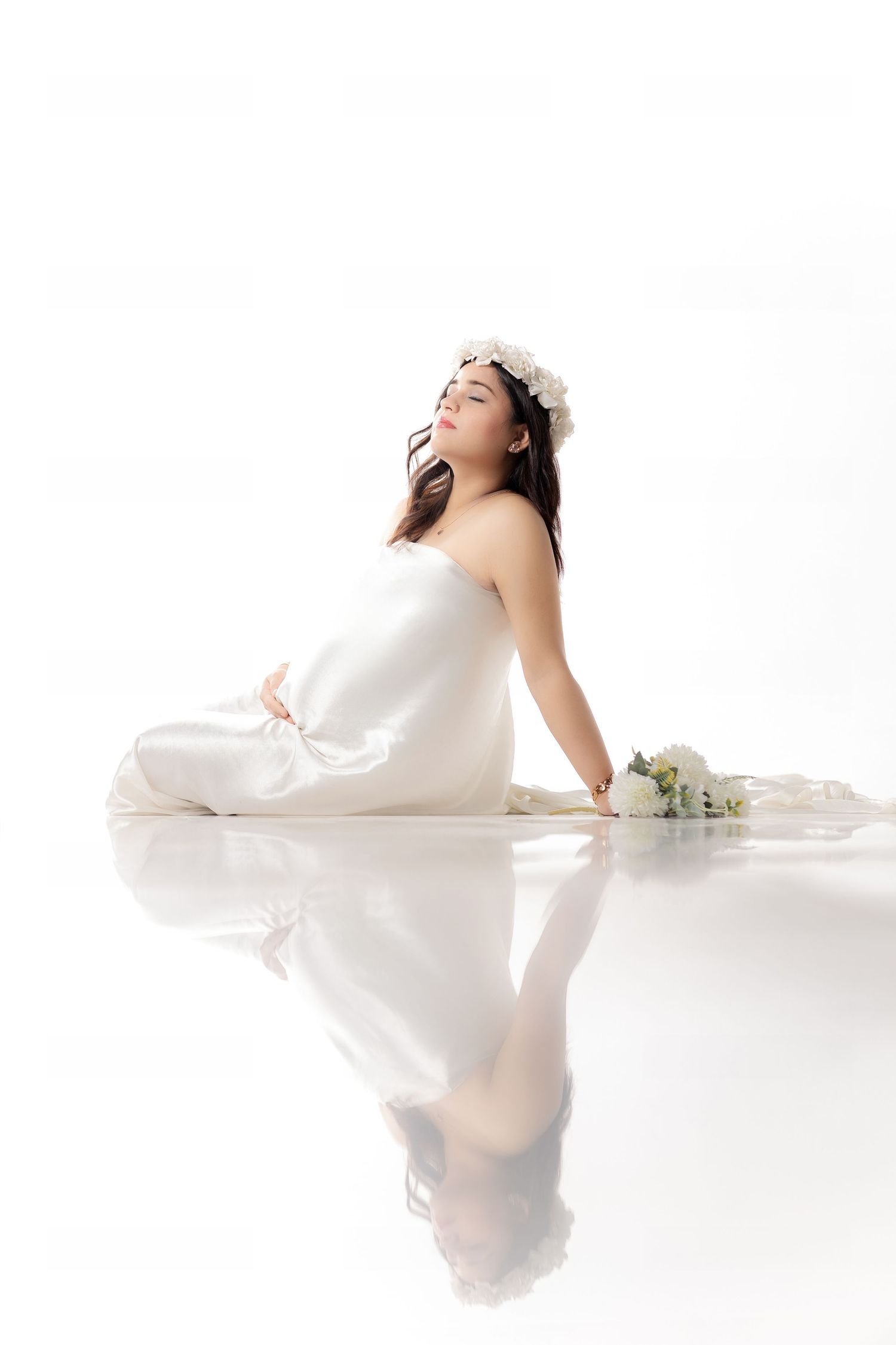 Artistic maternity photoshoot with white flowing fabric and soft reflections.