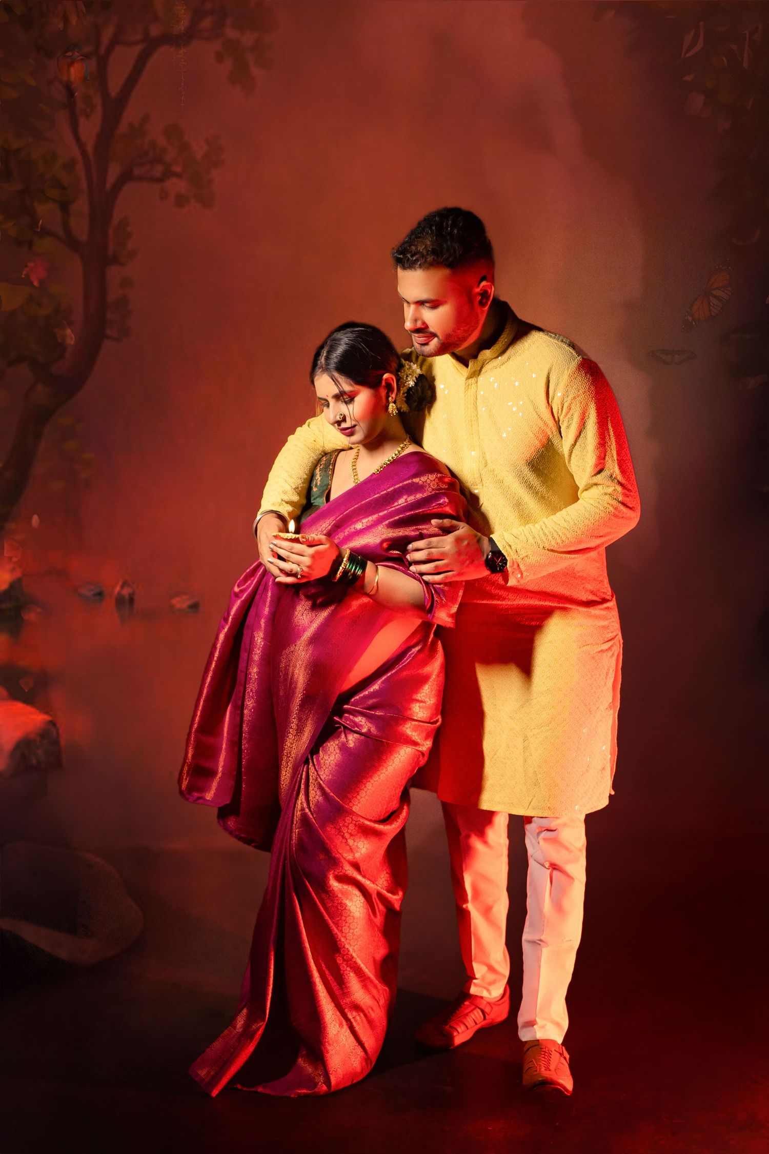 Couple in traditional Indian attire sharing intimate moment during maternity photoshoot with red lighting.