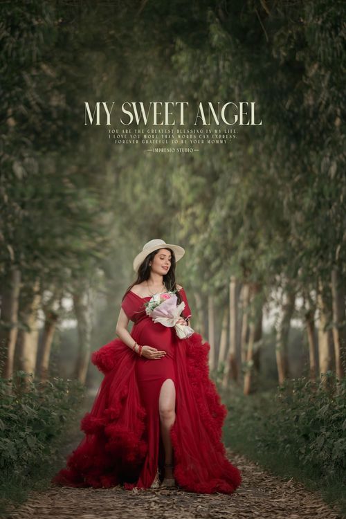 Figure in flowing red tulle dress and sunhat poses elegantly in a dreamy forest path holding white flowers.