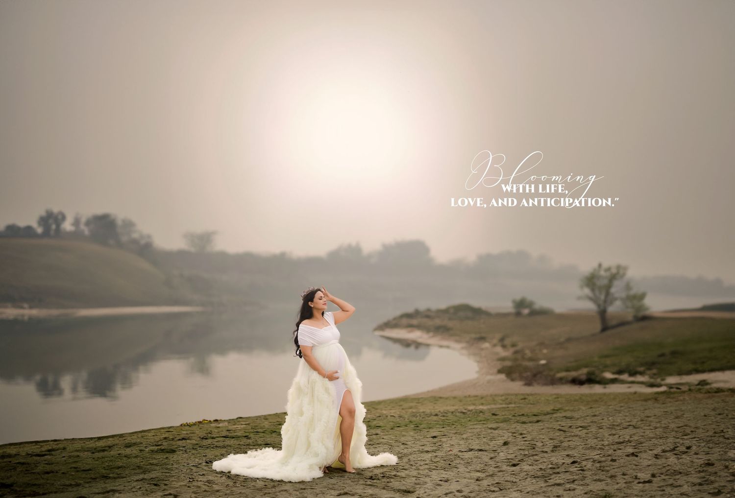 Pregnant woman in white gown poses by misty river at sunset in a dreamy maternity photography session.