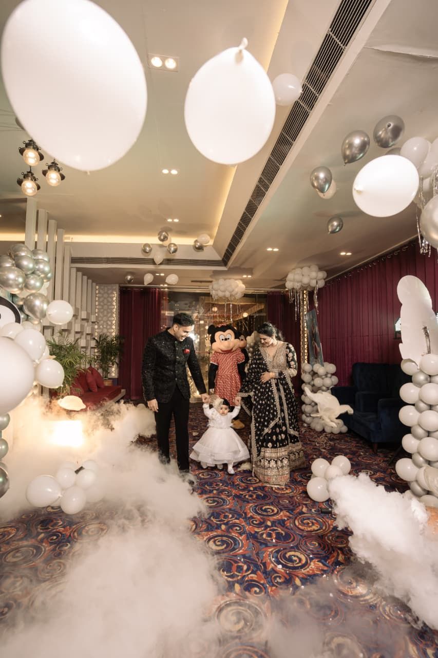 Family walking through dreamy balloon-filled venue with fog effects at Indian birthday party.