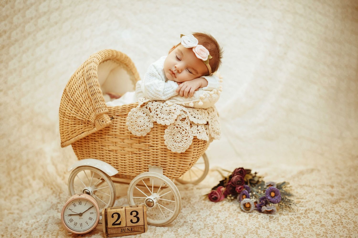Newborn baby sleeping peacefully in a vintage wicker pram with a clock and number blocks showing 23.