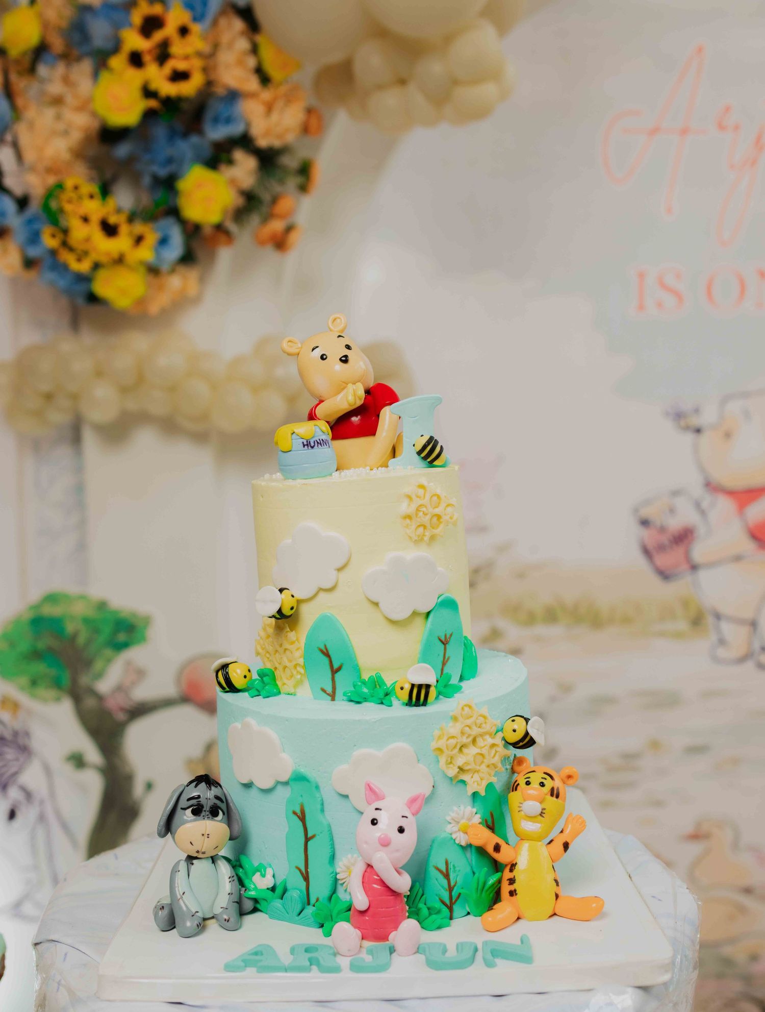 Three-tier Winnie the Pooh birthday cake with fondant characters including Tigger, Piglet, and Eeyore for Arjun.