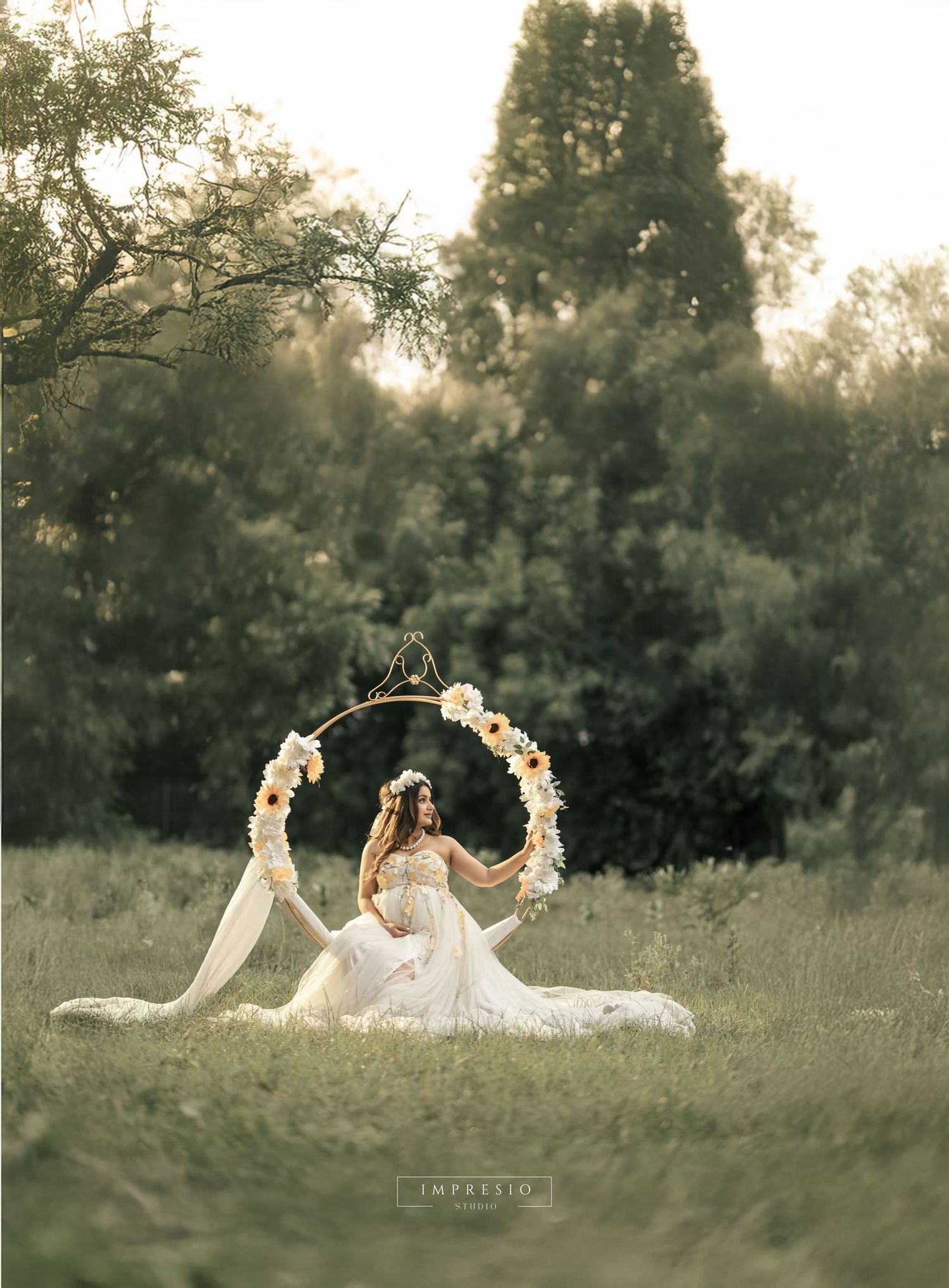 Ethereal maternity scene with flower wreaths in sunlit field.