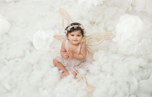 Angelic baby portrait with delicate wings against white cloud backdrop.