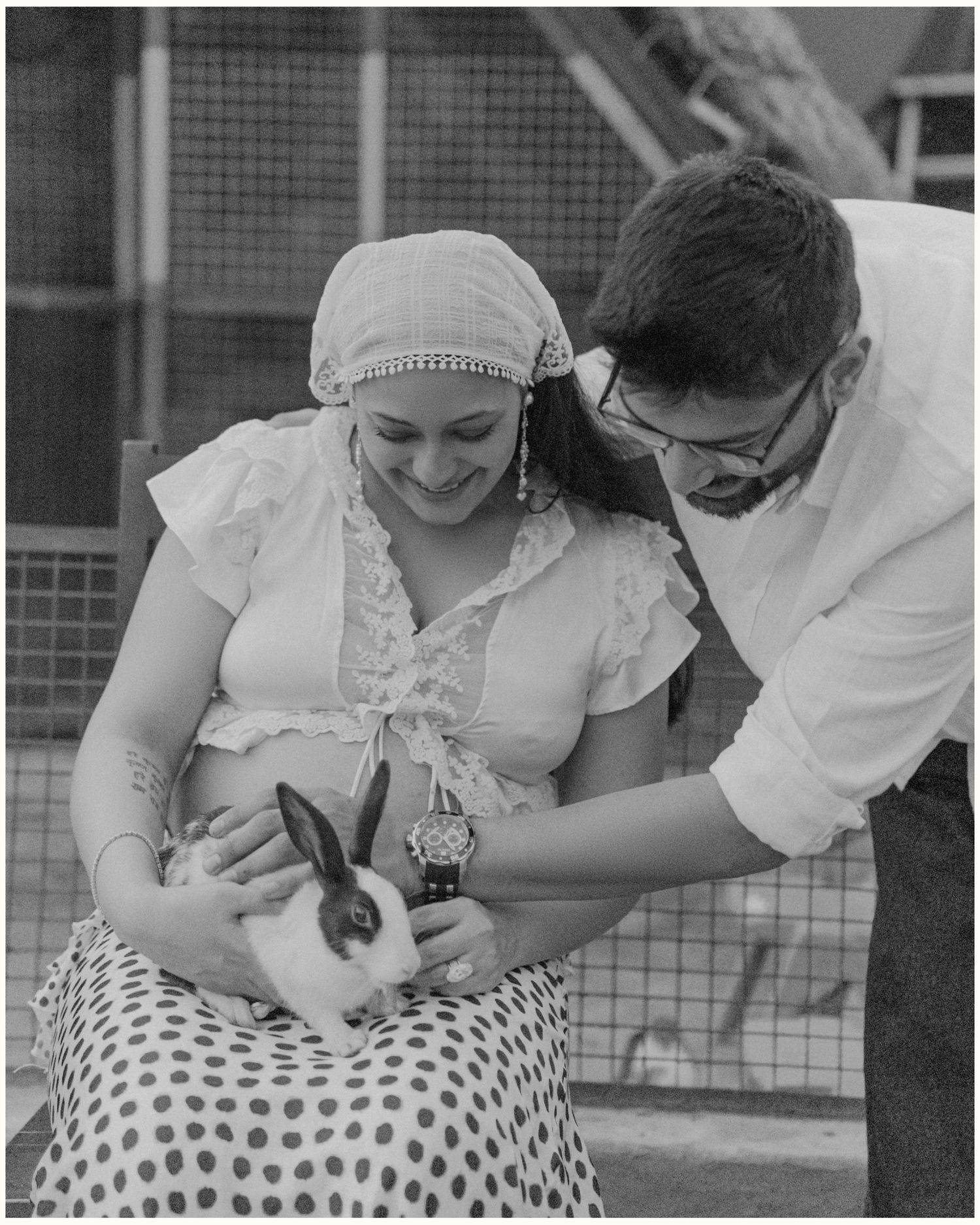 A woman in a headscarf and man with glasses tenderly hold a white rabbit together in a black and white photo.