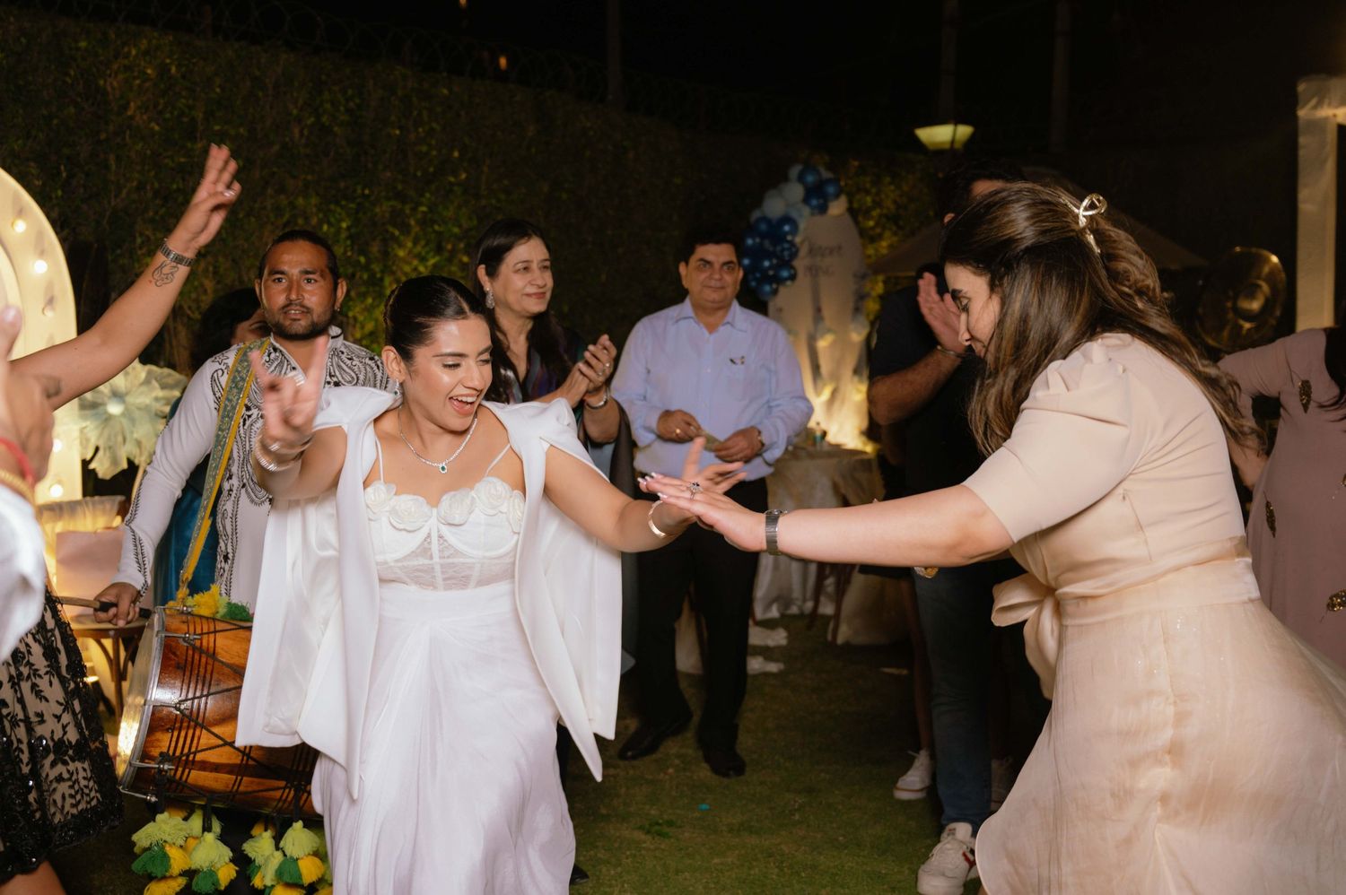Bride in white dress dancing joyfully with guests at an outdoor evening wedding celebration.