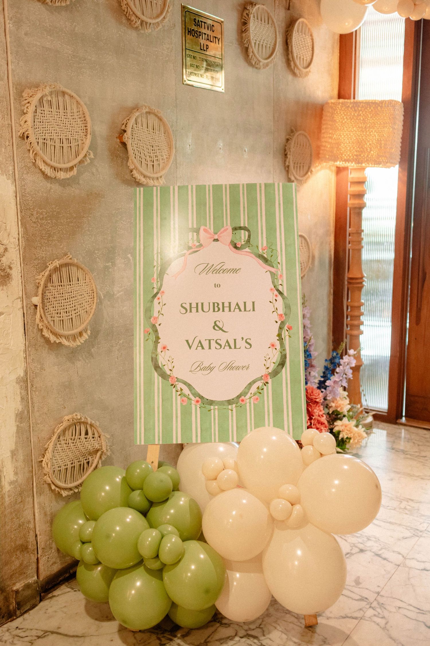 Baby shower welcome sign for Shubhali & Vatsal decorated with green and cream balloons and floral accents.