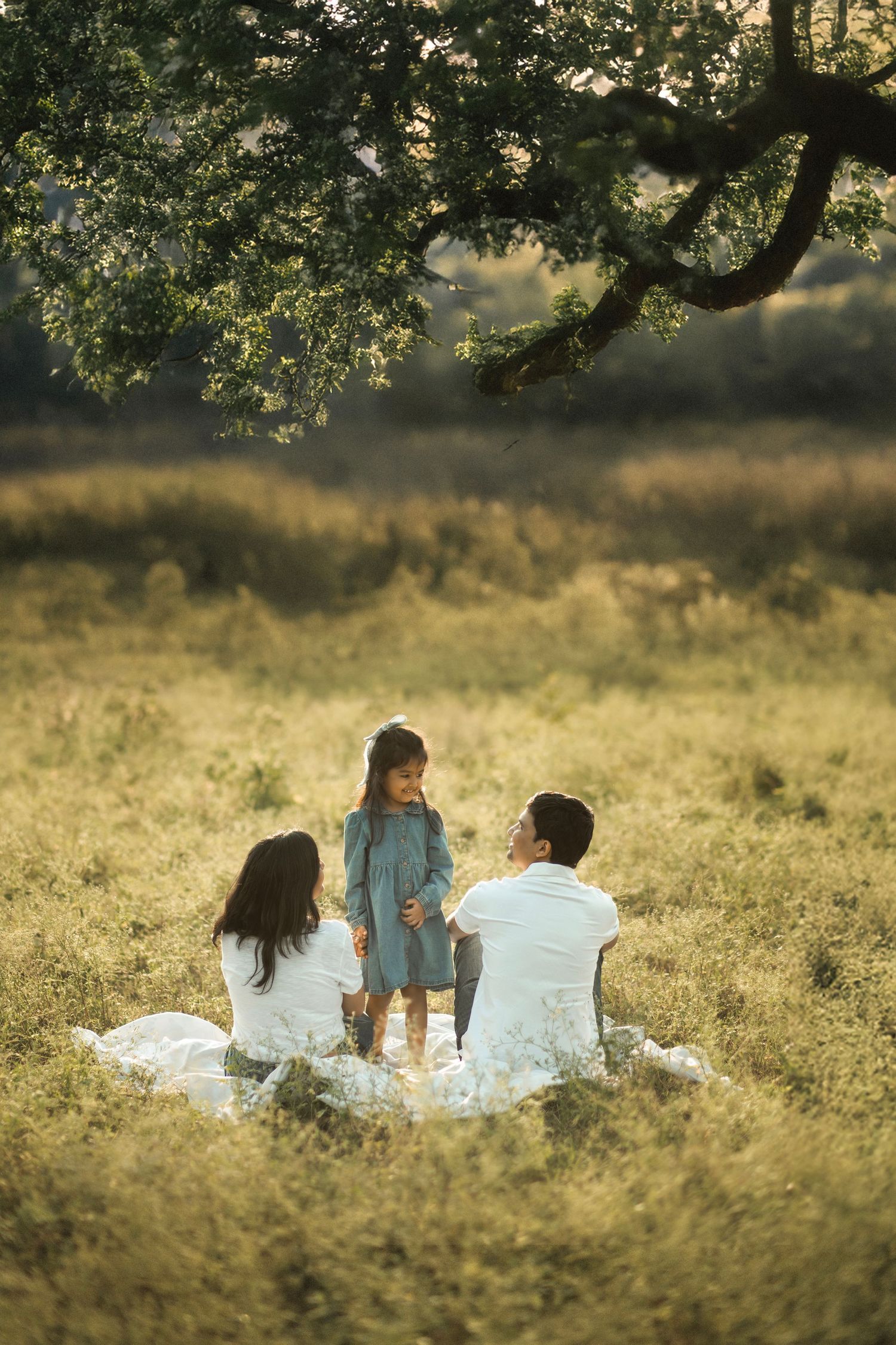 Three people relax together on a blanket in a sunlit meadow during golden hour.