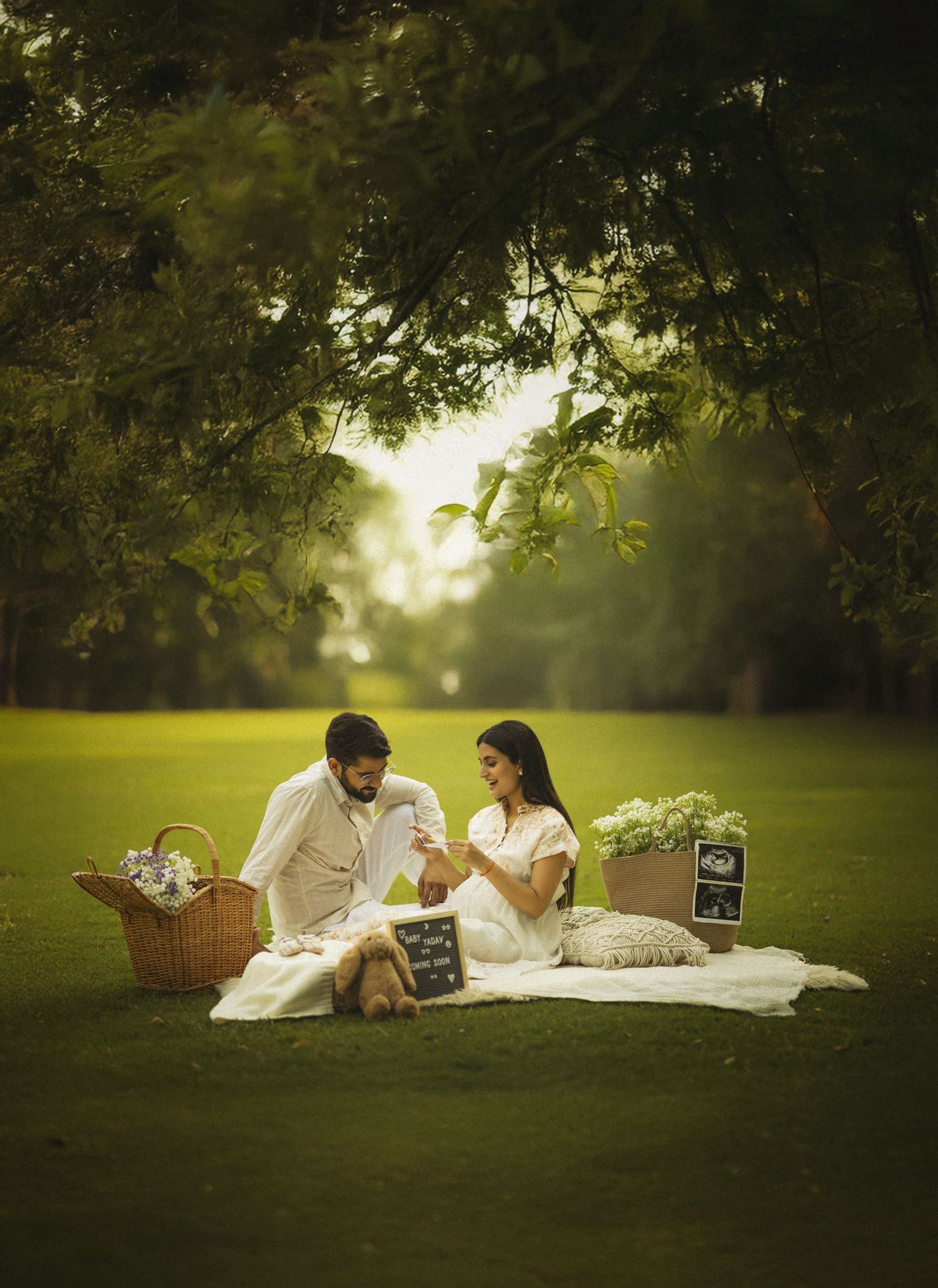A romantic picnic scene in a lush green garden with blanket, basket and chalkboard signs under overhanging tree branches.