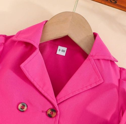 Close-up of a bright pink collared jacket with decorative buttons on a wooden hanger.