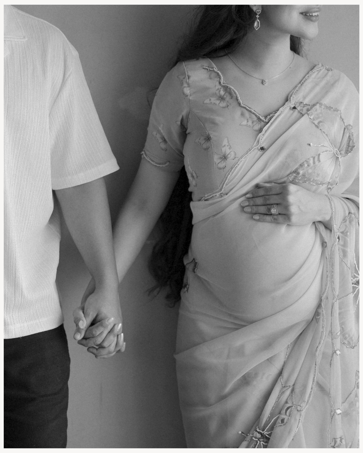 Black and white maternity photo of pregnant woman in saree holding hands with partner.