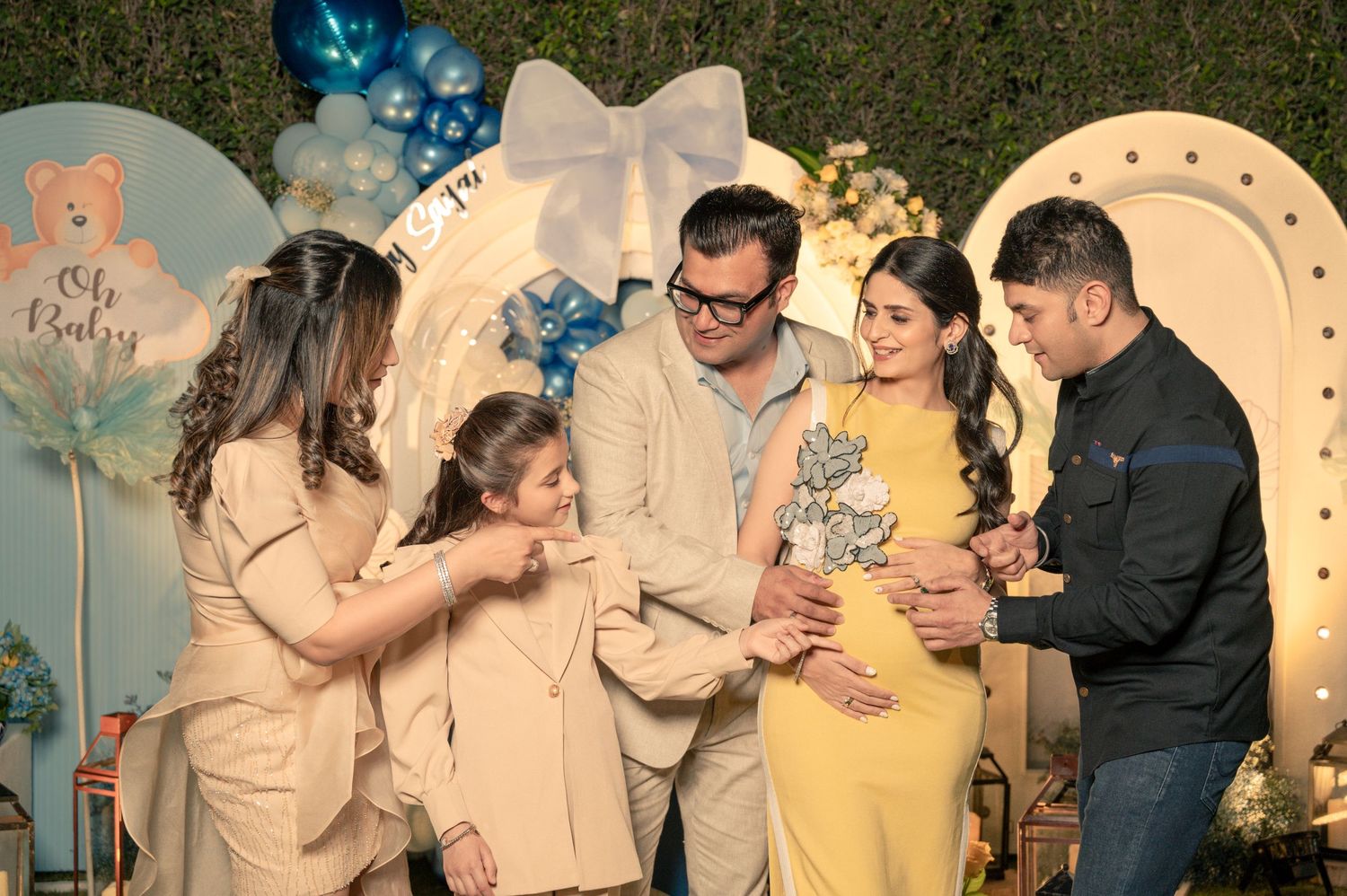 Family celebrating a baby shower with blue balloons and teddy bear decorations at an outdoor evening party.