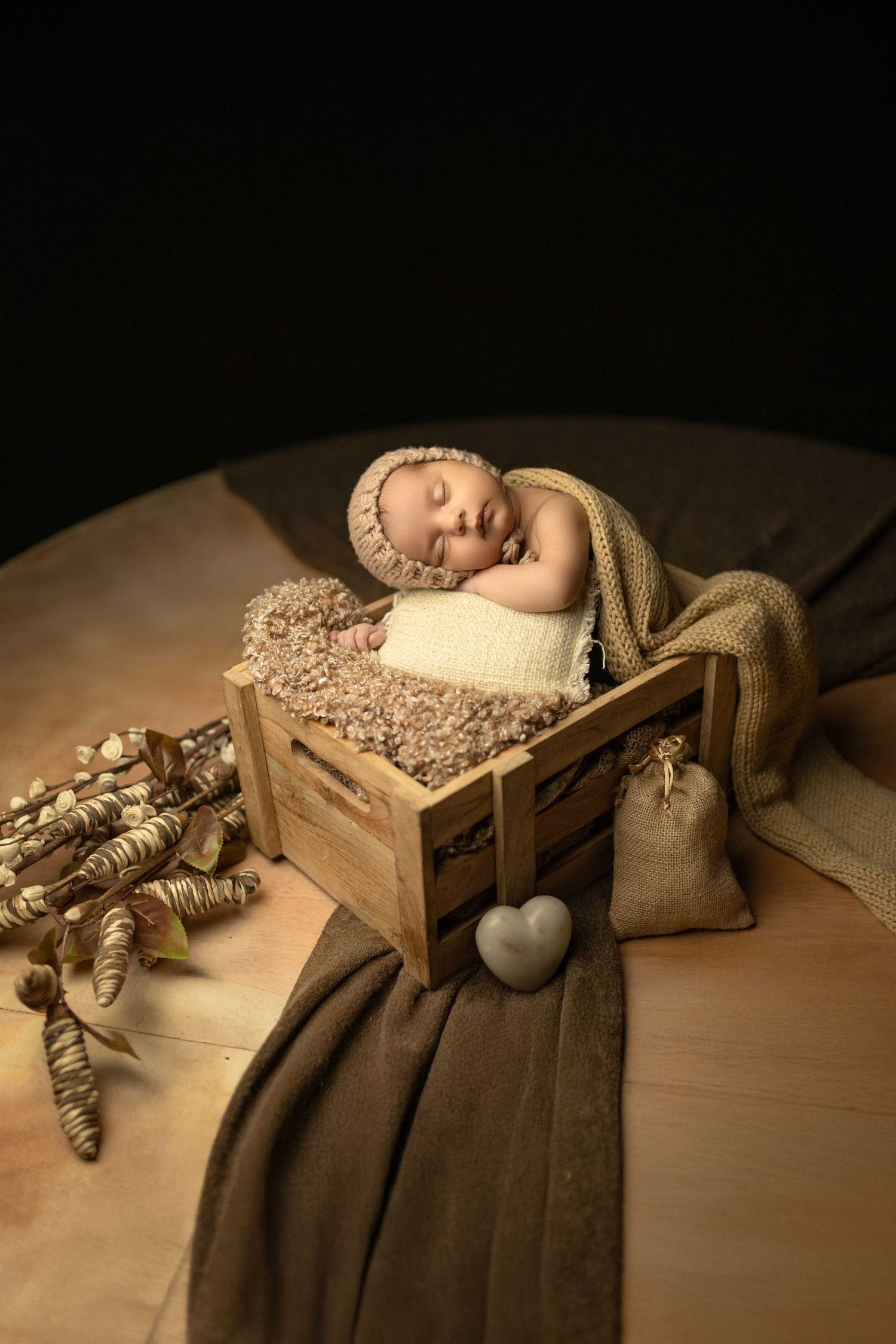 Peaceful newborn baby sleeping in a rustic wooden crate with soft beige knit wrap and bonnet, surrounded by natural decor.
