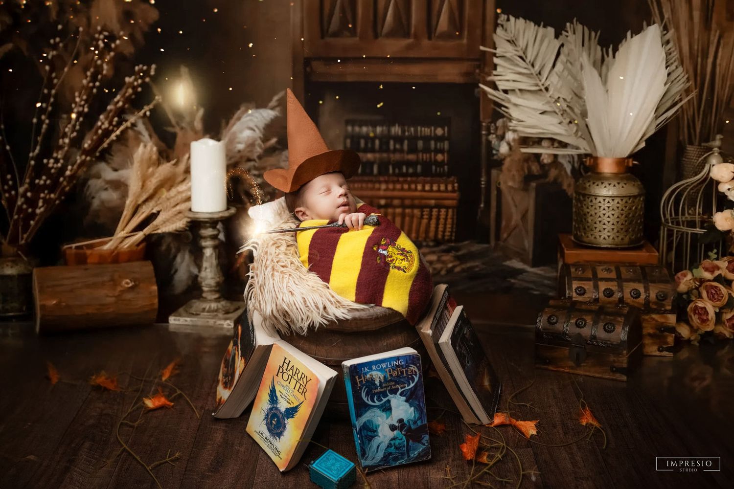 Newborn baby in Harry Potter witch hat and Gryffindor scarf sleeping in a cauldron surrounded by spell books.