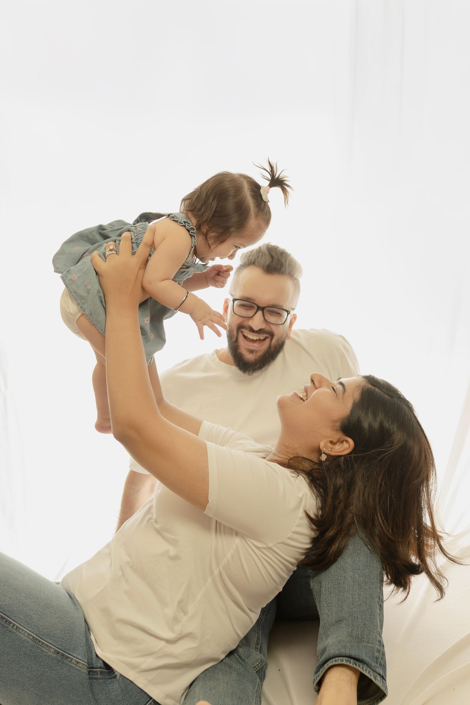 A family plays together joyfully on a white background, lifting and embracing in a series of candid moments.