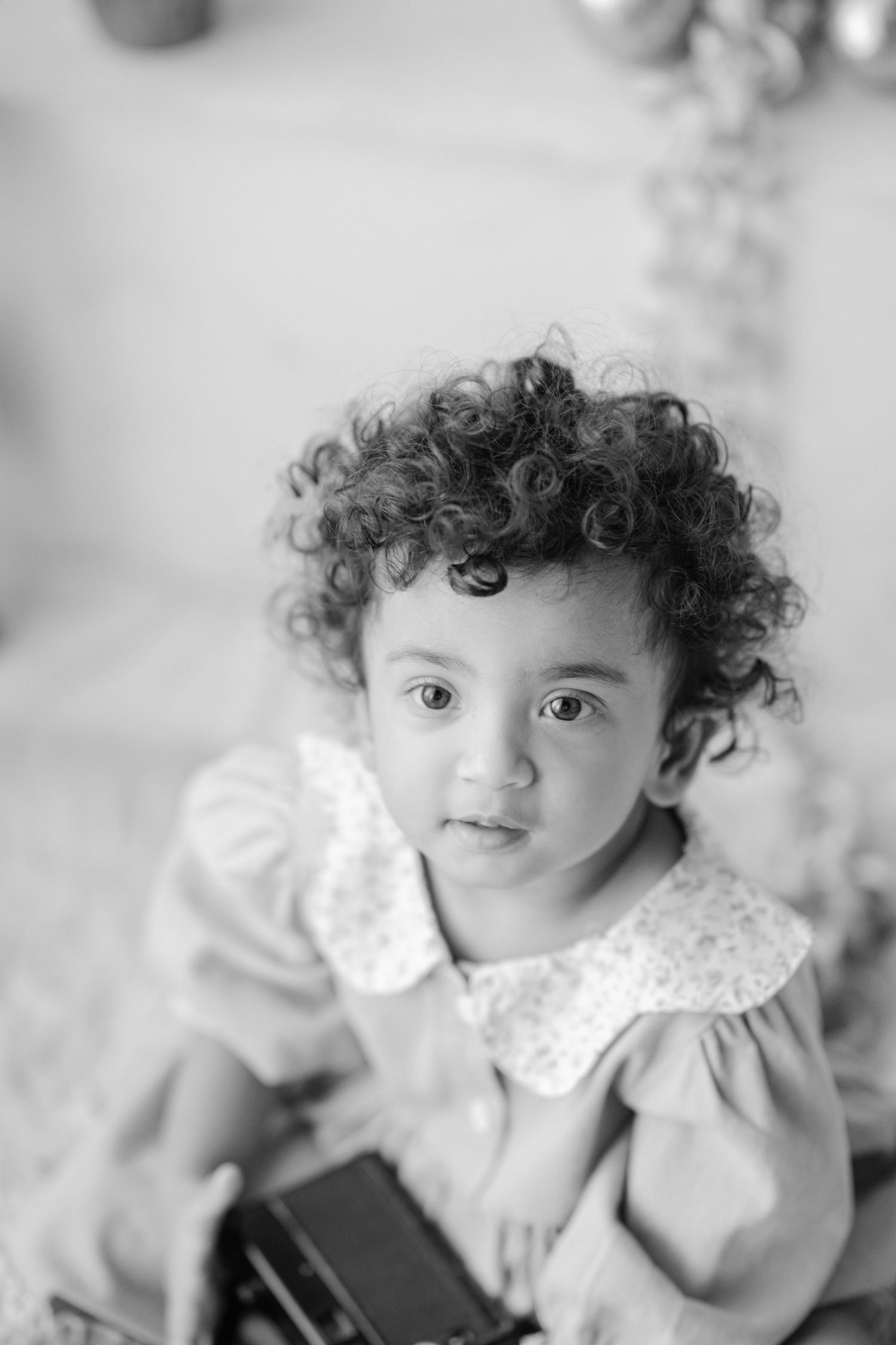 Black and white portrait of a cute toddler girl with curly hair wearing a dress with floral collar.