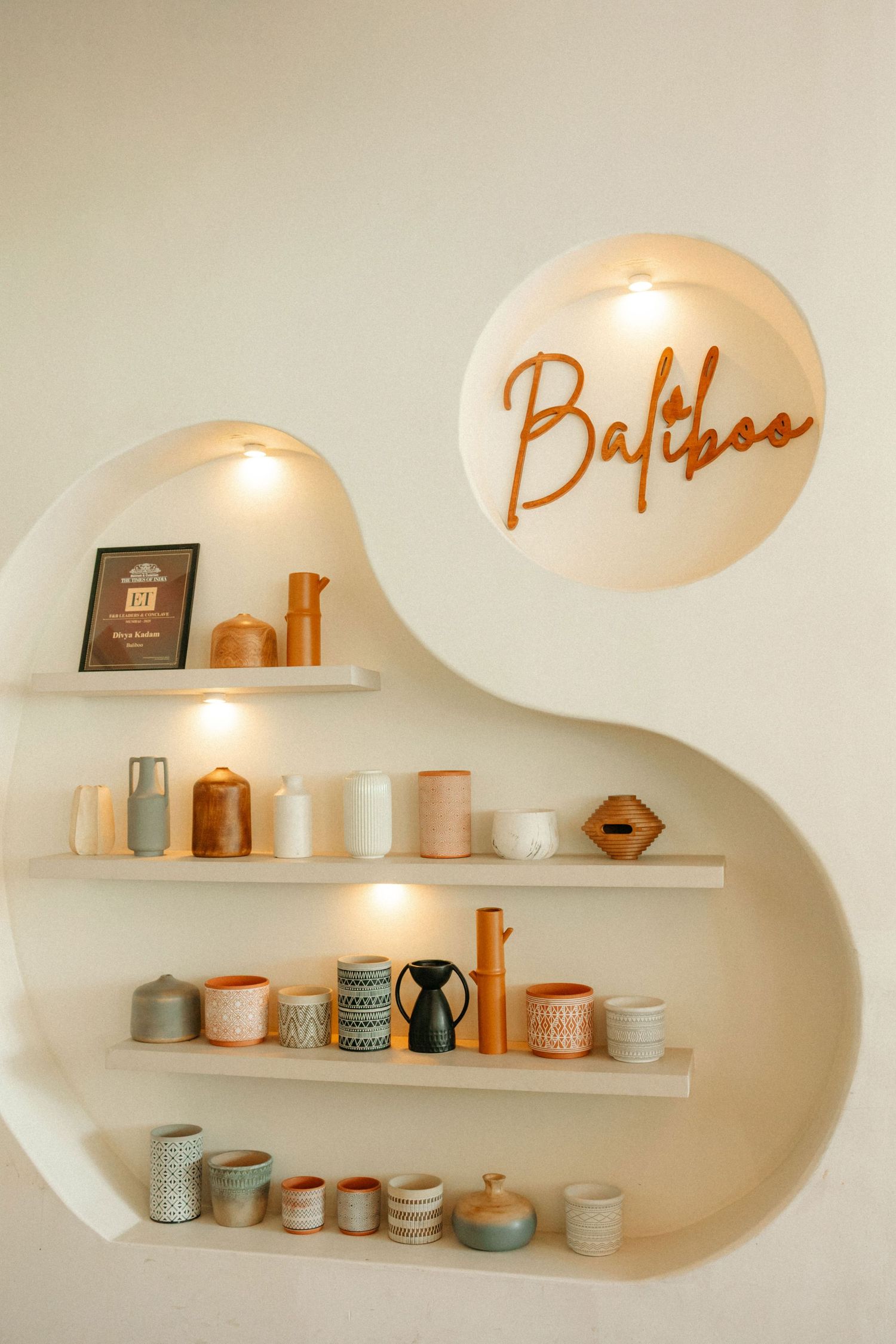 Baltboo branded wall shelves displaying handmade ceramic mugs, vases, and pottery in neutral tones with warm accent lighting.