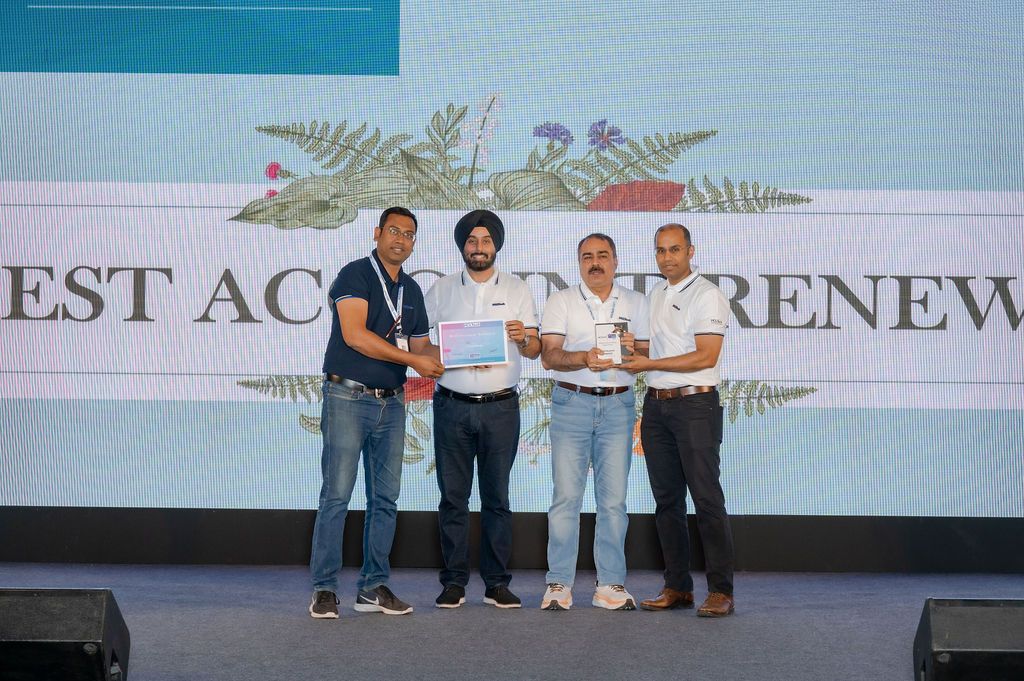 A group stands together on stage at an awards ceremony with a banner displaying 'EST AC RENEW' in the background.