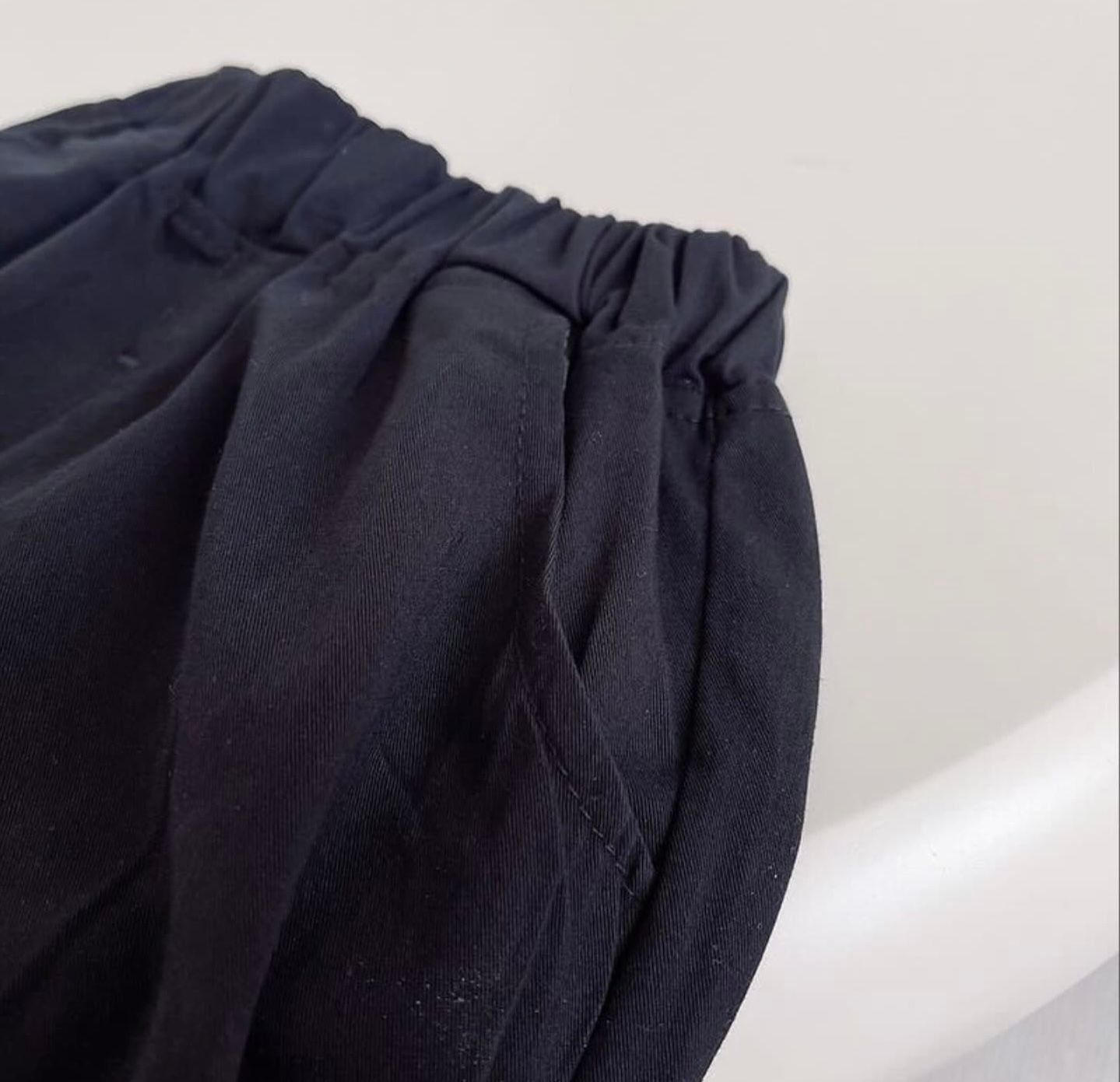 Closeup view of gathered black fabric showing shirring details and texture on a white surface.