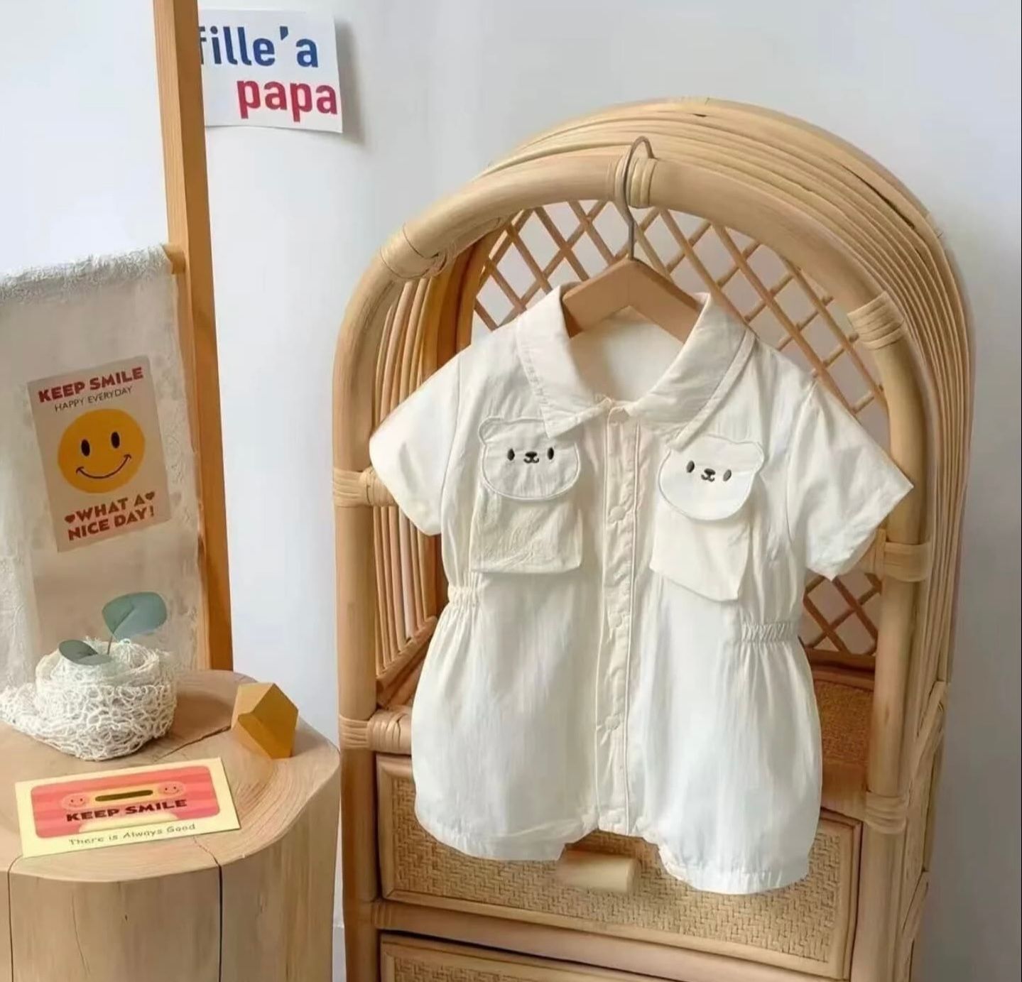 A collection of white vintage baby clothing and accessories displayed on a rattan chair against a neutral background.