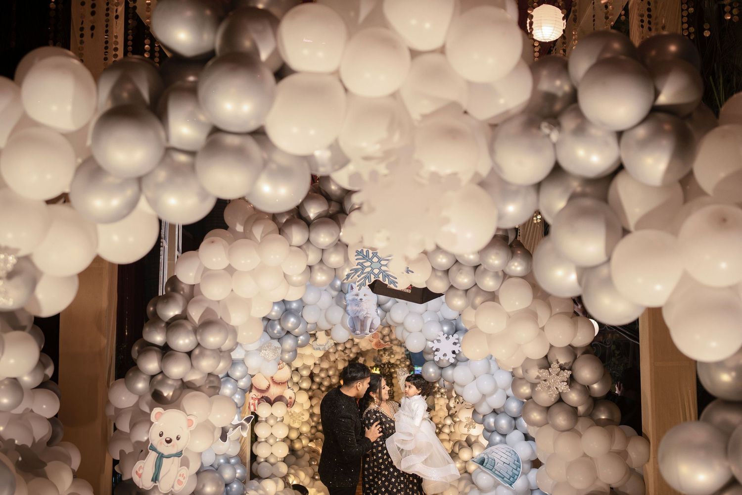 Romantic couple poses under stunning white and silver balloon arch wedding backdrop with floral decorations.