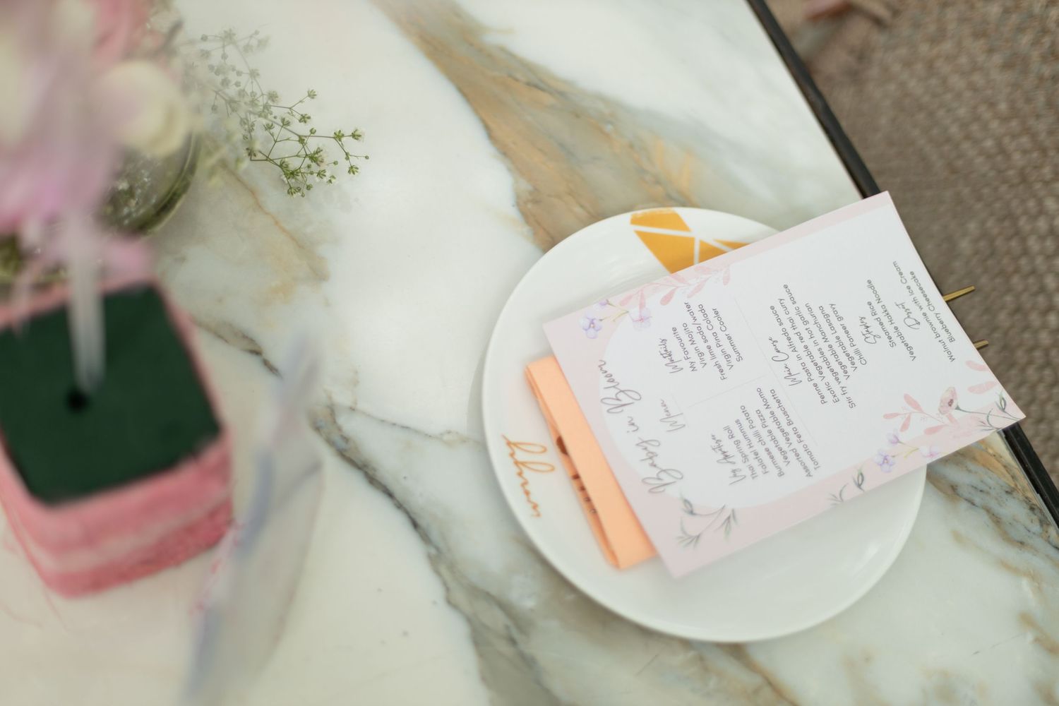 Elegant wedding menu cards on a marble table with peach accents, floral details, and a white ceramic plate.