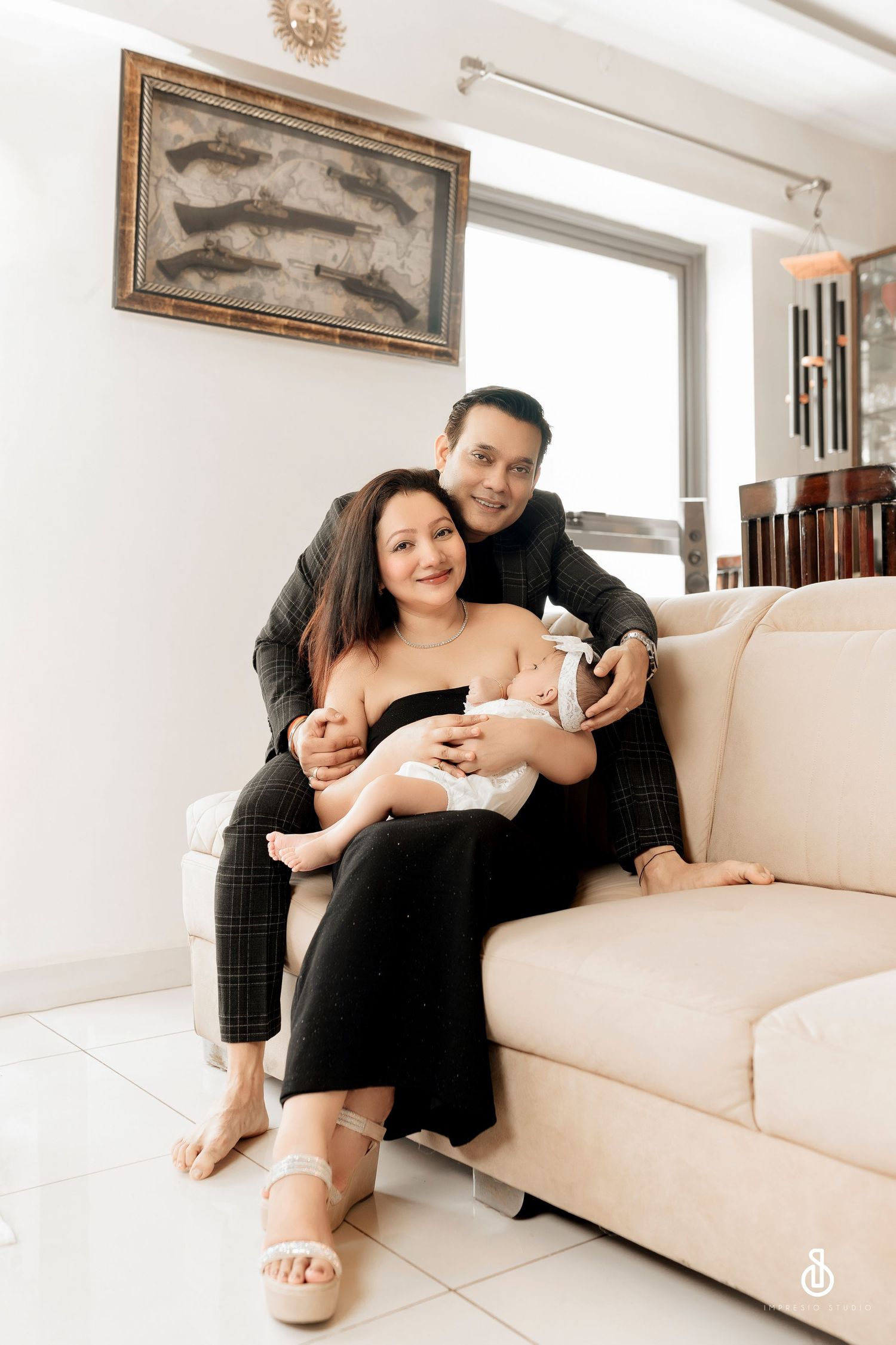 Happy couple sitting on a cream sofa holding their newborn baby in a bright, modern living room.