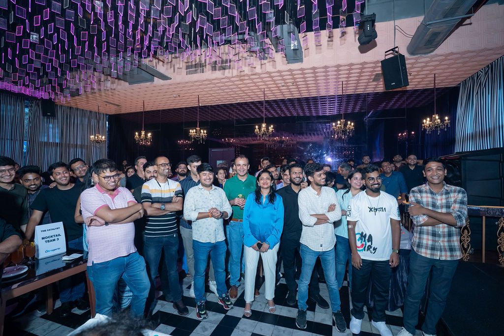 Large group of people posing together in a nightclub with chandeliers and purple lighting overhead.