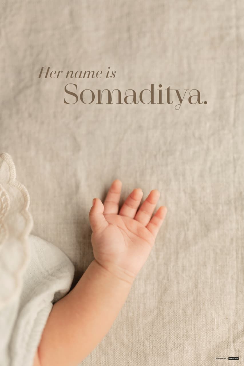 A newborn baby's tiny hand rests on a linen background with the text Her name is Somaditya.