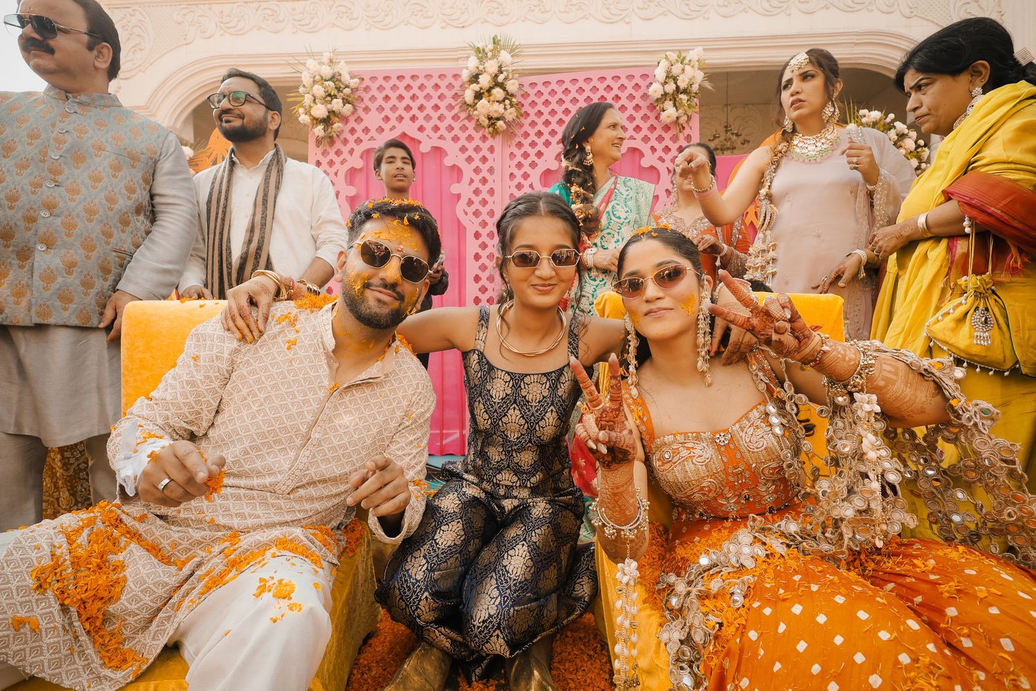 Joyful Indian wedding celebration with guests in vibrant orange and gold traditional attire at a colorful mehndi ceremony.