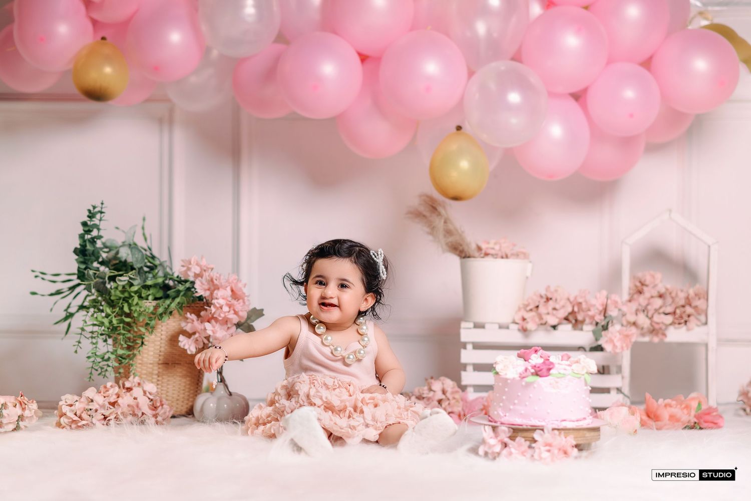 Pink and white balloon garland decorates a cake smash photo setup with floral arrangements and delicate party decor.