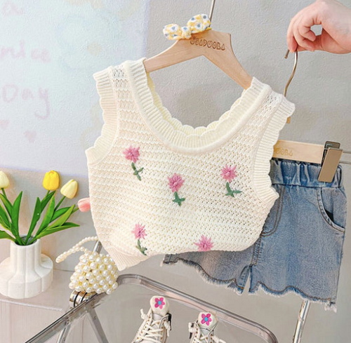 White crochet crop top with pink flower embroidery paired with denim shorts and white sneakers.