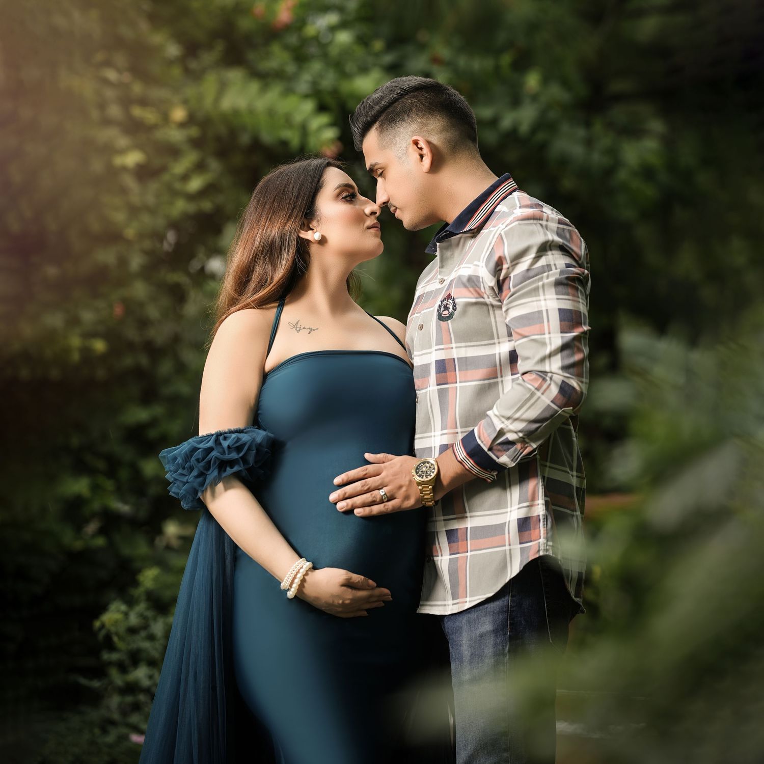 Outdoor maternity session with couple in blue dress and plaid shirt among greenery.