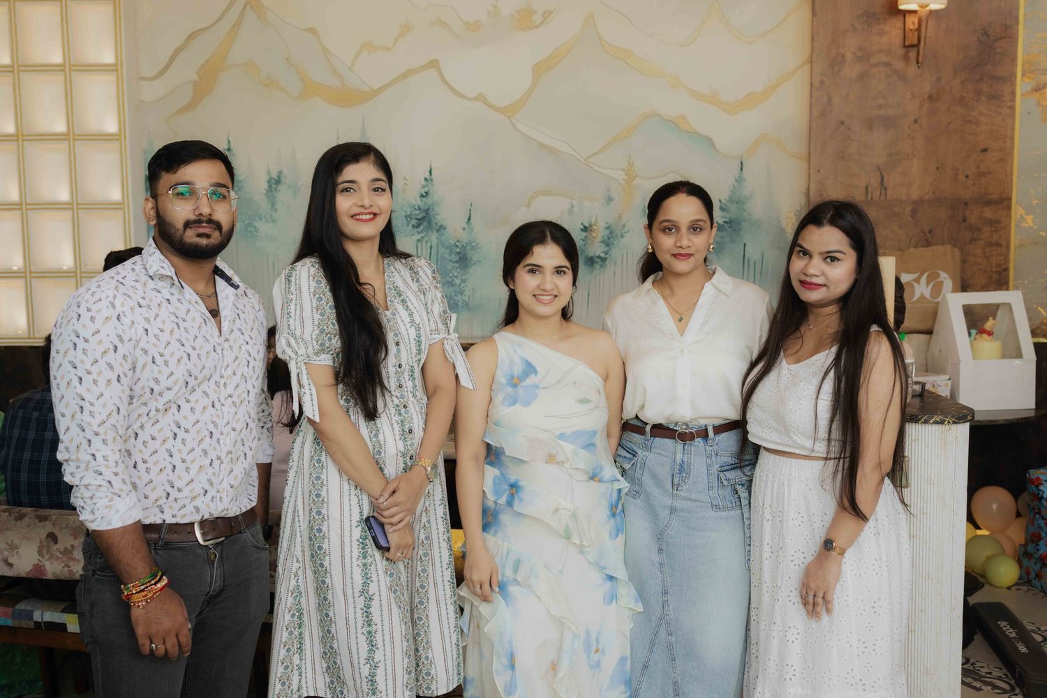 Five people posing together at an indoor celebration with watercolor mountain mural backdrop.