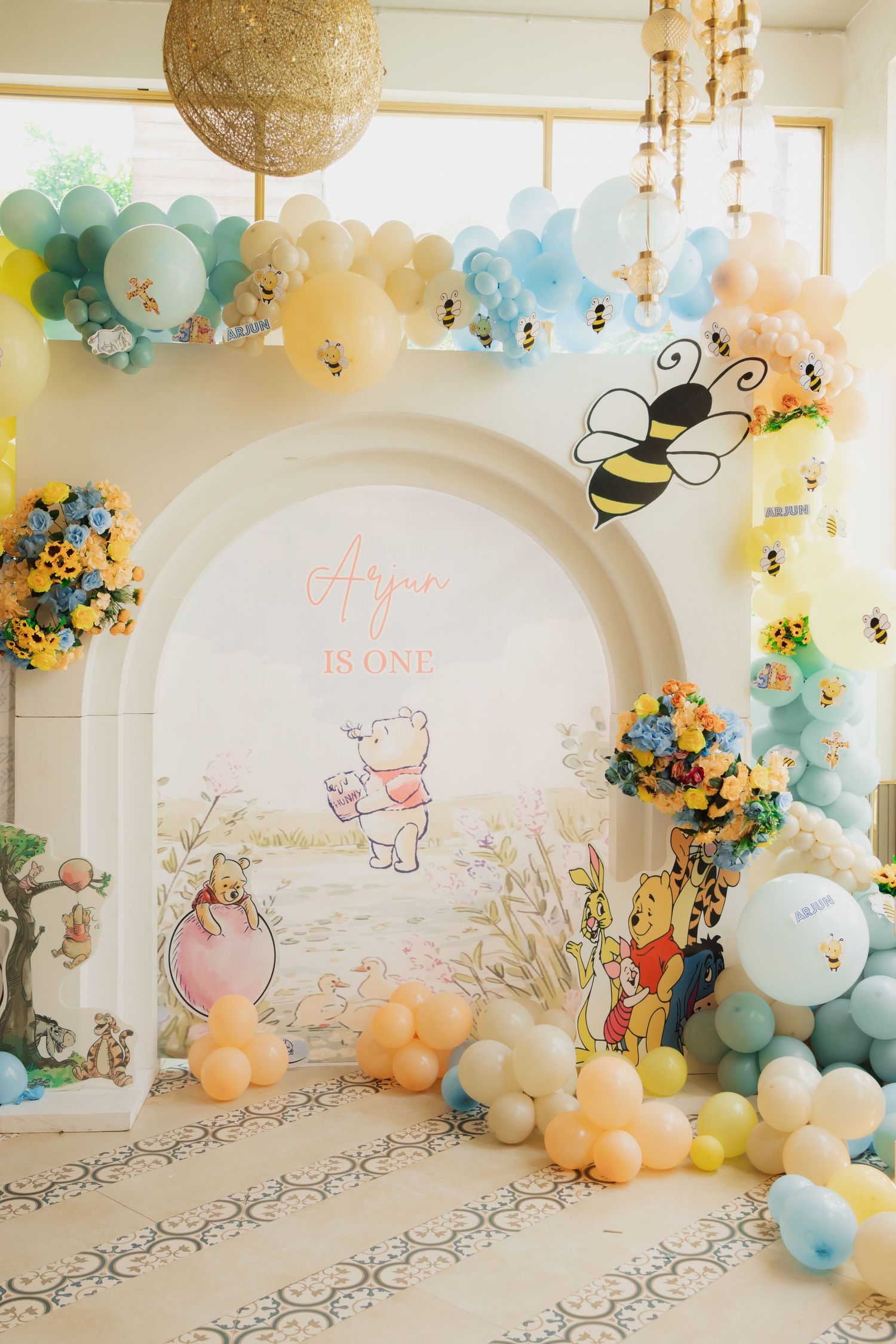 Winnie the Pooh first birthday party backdrop with pastel balloons, bee decorations, and floral arrangements.