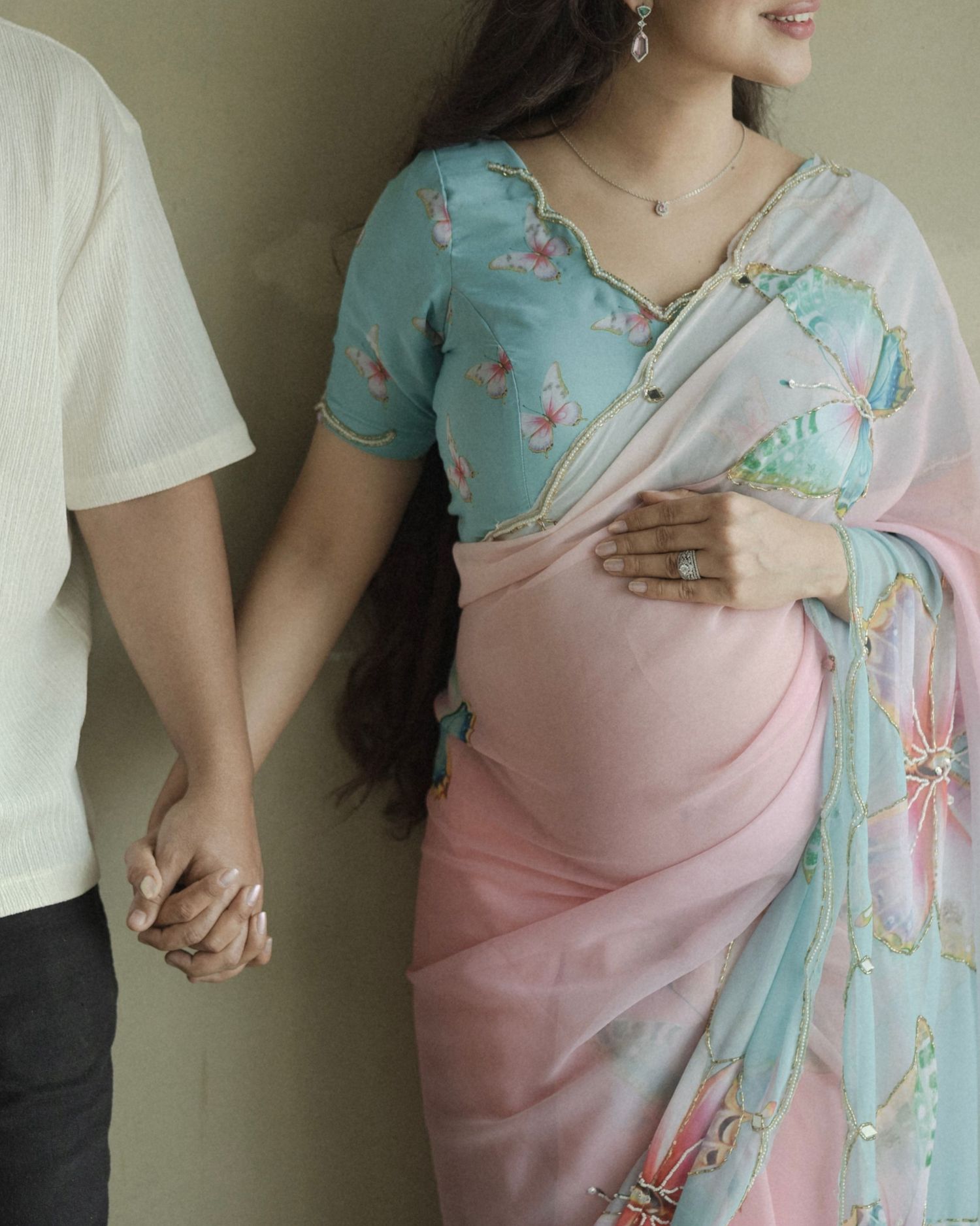 Pregnant woman in pink saree and blue blouse holds hands with partner during maternity photoshoot.