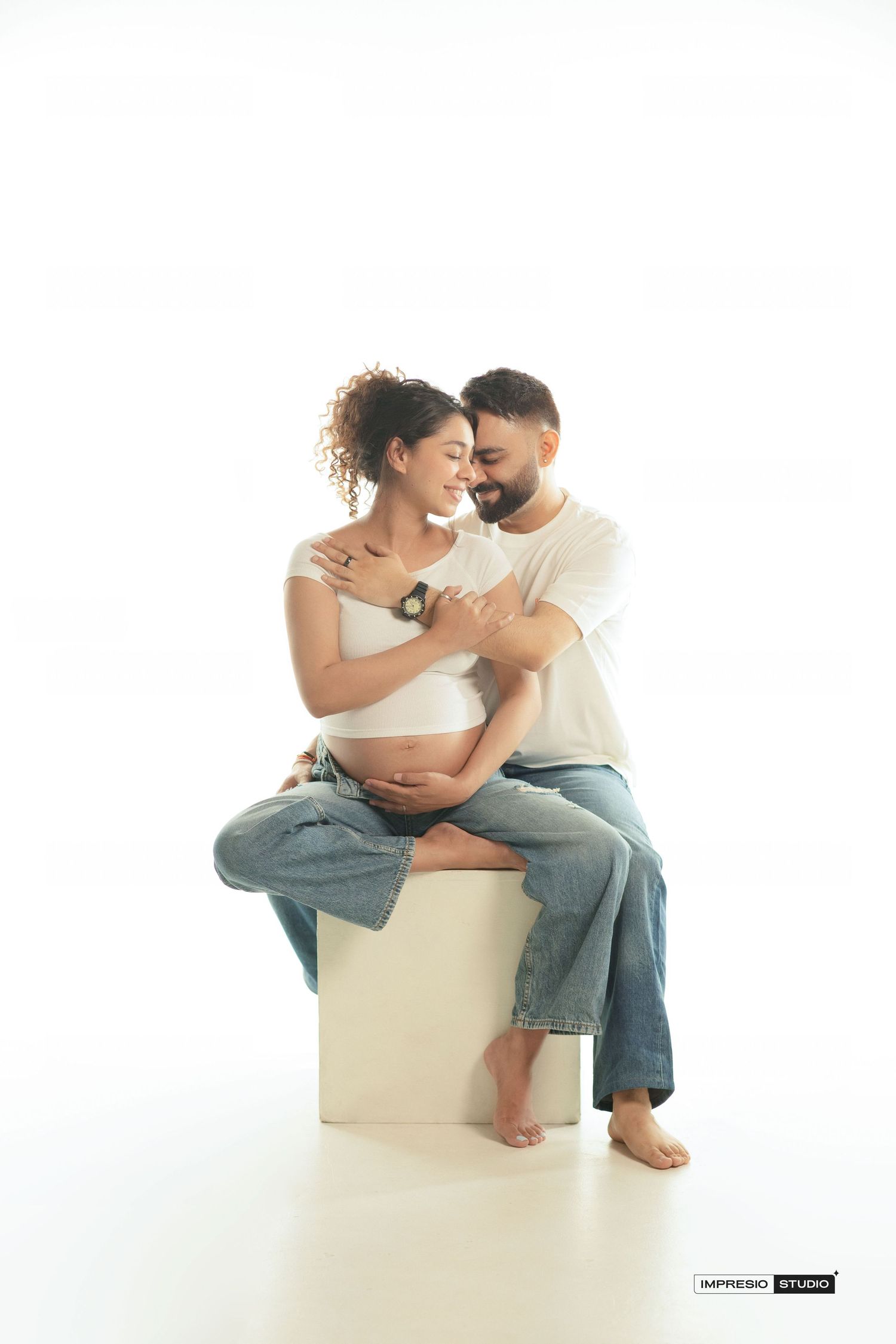 A pregnant woman and her partner share a tender embrace during a maternity photo shoot at Impresski Studio.