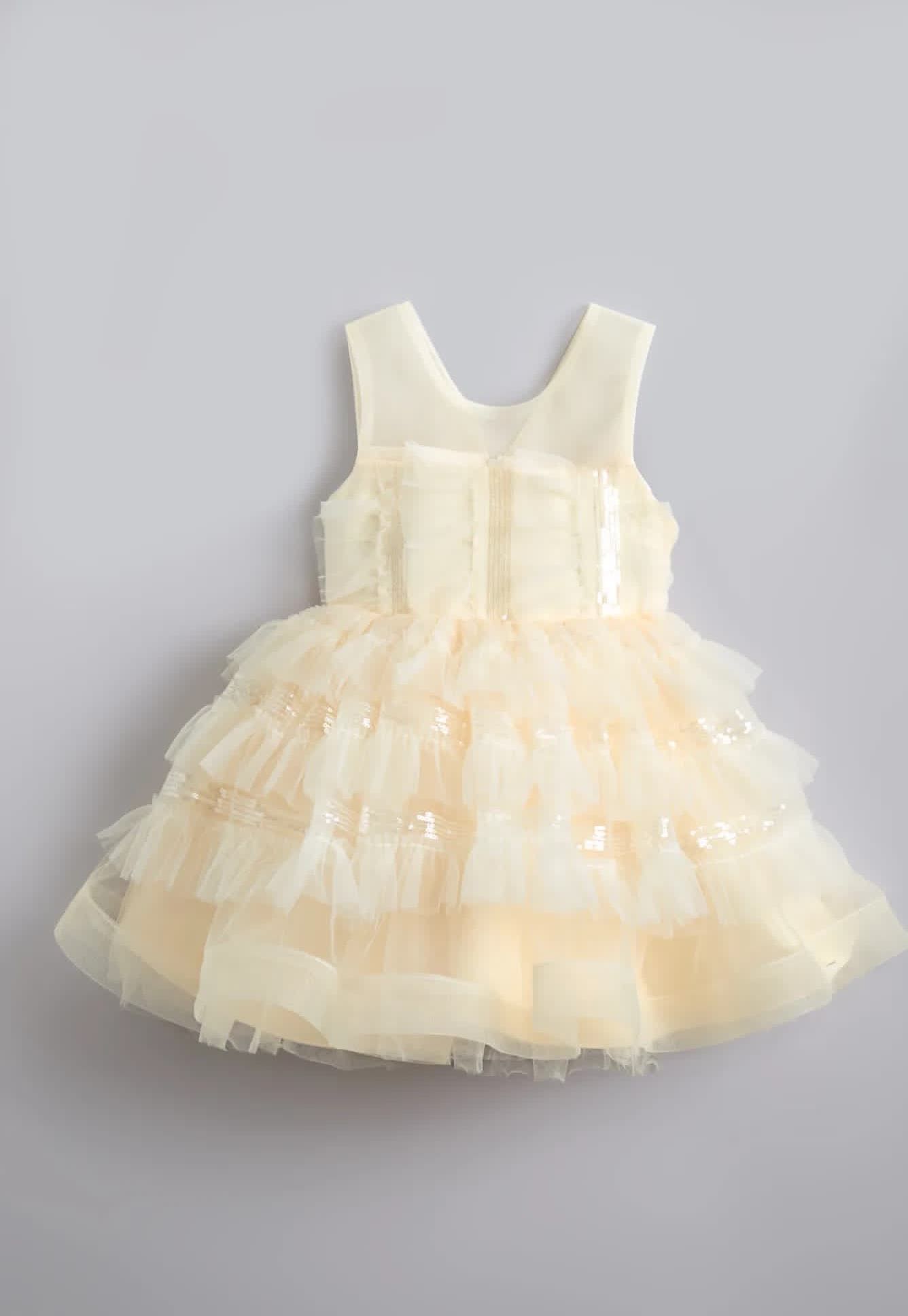 Baby dress with layers of cream-colored tulle ruffles shown at different angles against a gray background.