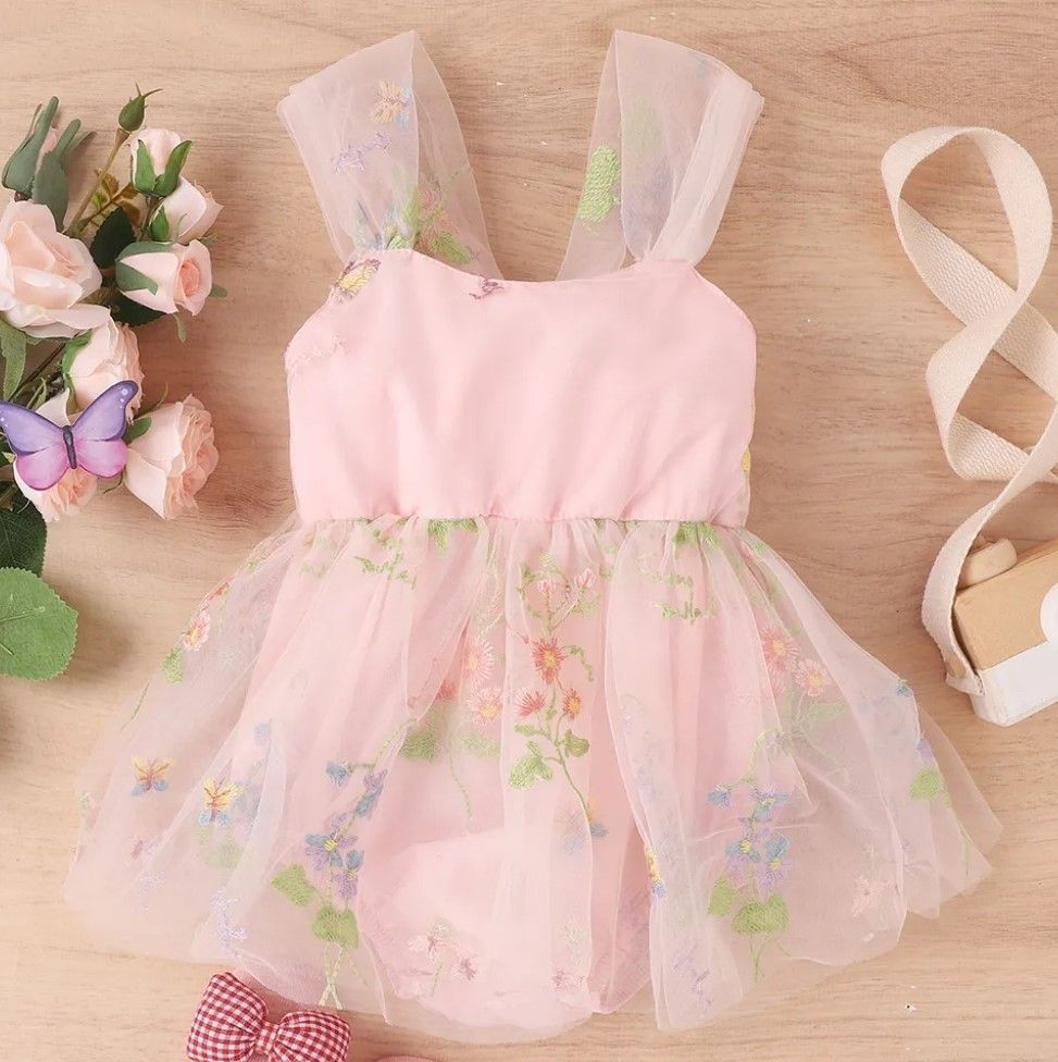 Pink tulle baby dress with floral embellishments displayed on wooden background.