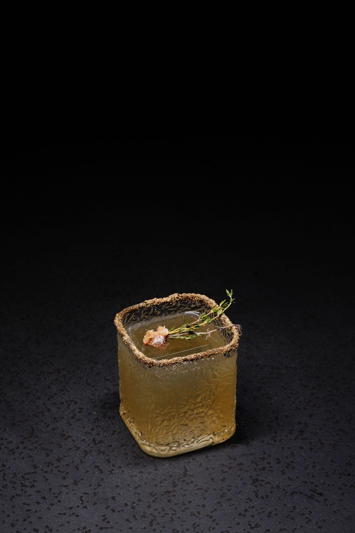Elegant cocktail with brown sugar rim and garnish served on dark surface with water droplets.